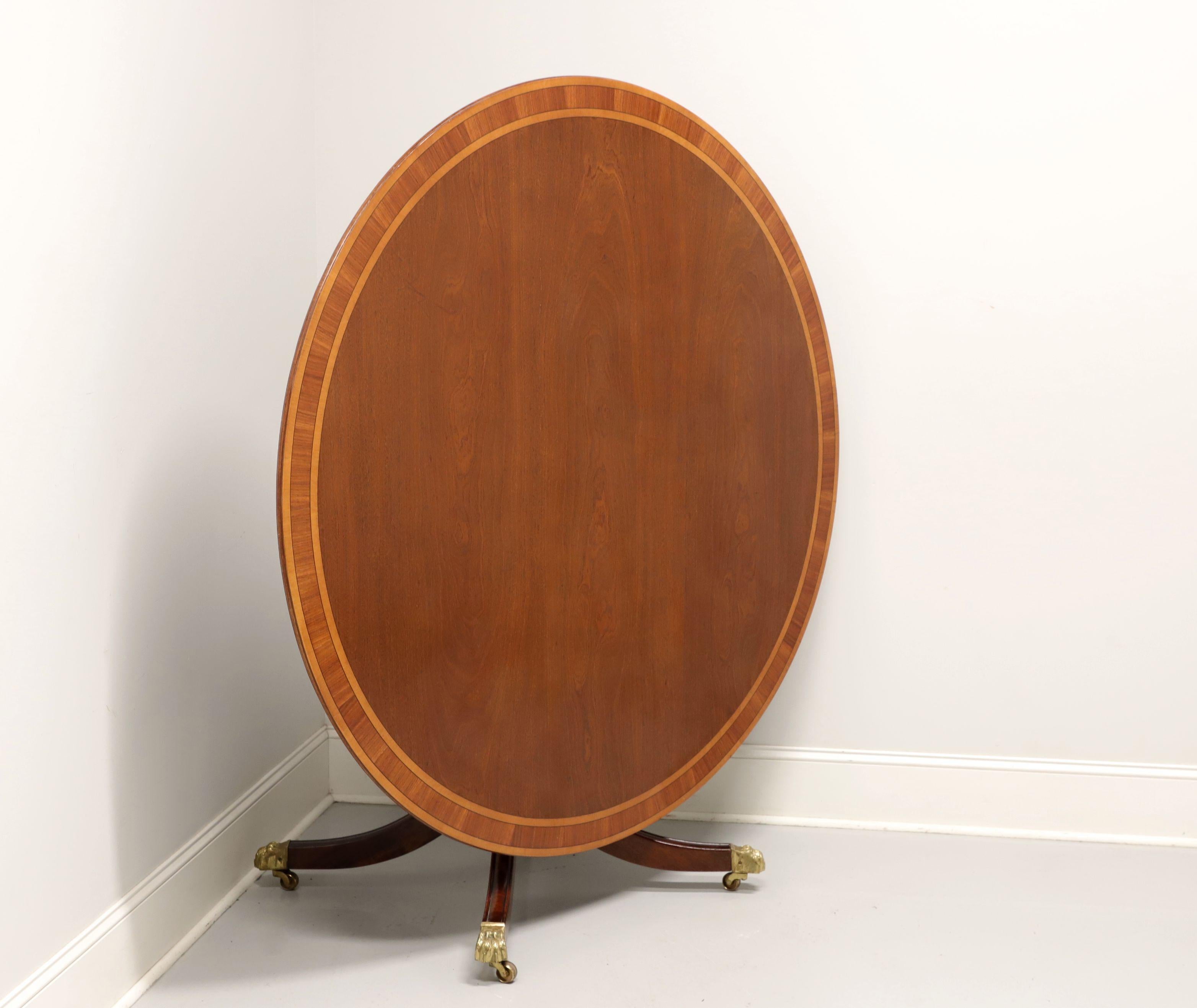 A 20th century reproduction of an Edwardian style tilt-top 60 inch round dining table, unbranded. Mahogany and satinwood with veneers, banded top, ribbed edge, single pedestal with turned base, four legs and brass paw toe caps with casters. A pivot