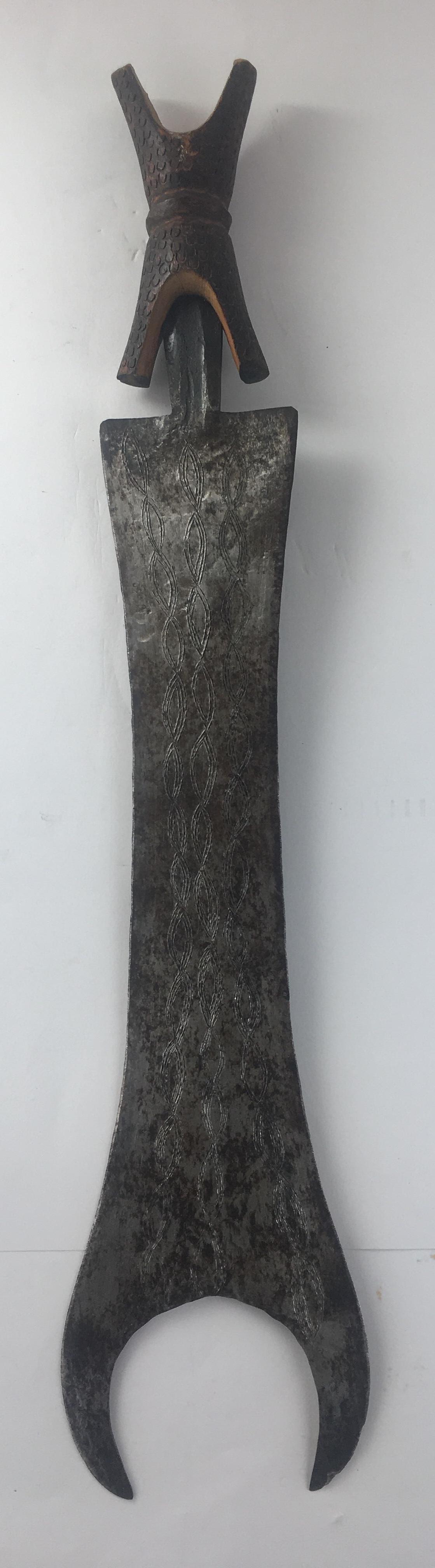 Épée de cérémonie africaine de la République démocratique du Congo, vers les années 1920. Du fer et du bois, dans un étui fait de tissu et de peau d'animal.

Cette épée tribale, symbole de statut, est portée par une lame de fer à bord unique, gravée