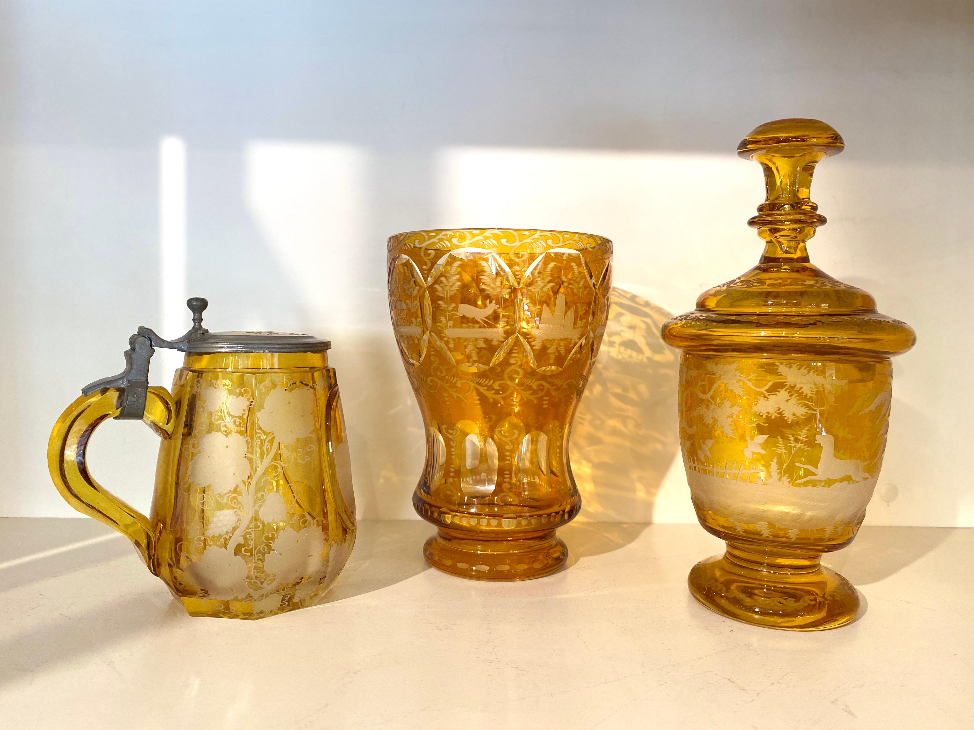 Vetro ceco di Boemia, vasi e brocca giallo-ambra, incisi a mano e decorati con alberi, uccelli e cervi tutt'intorno. Circa 1920. 