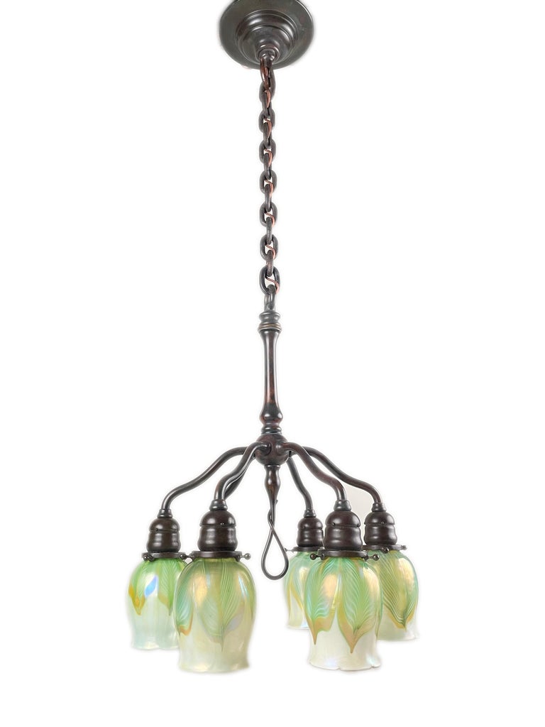A early 20th century American Art Nouveau cast bronze and favrile glass Six Light Chandelier by, Tiffany Studios decorated with six blown iridescent pulled feather decorated Tiffany Favrile art glass shades further suspended from a cast bronze and