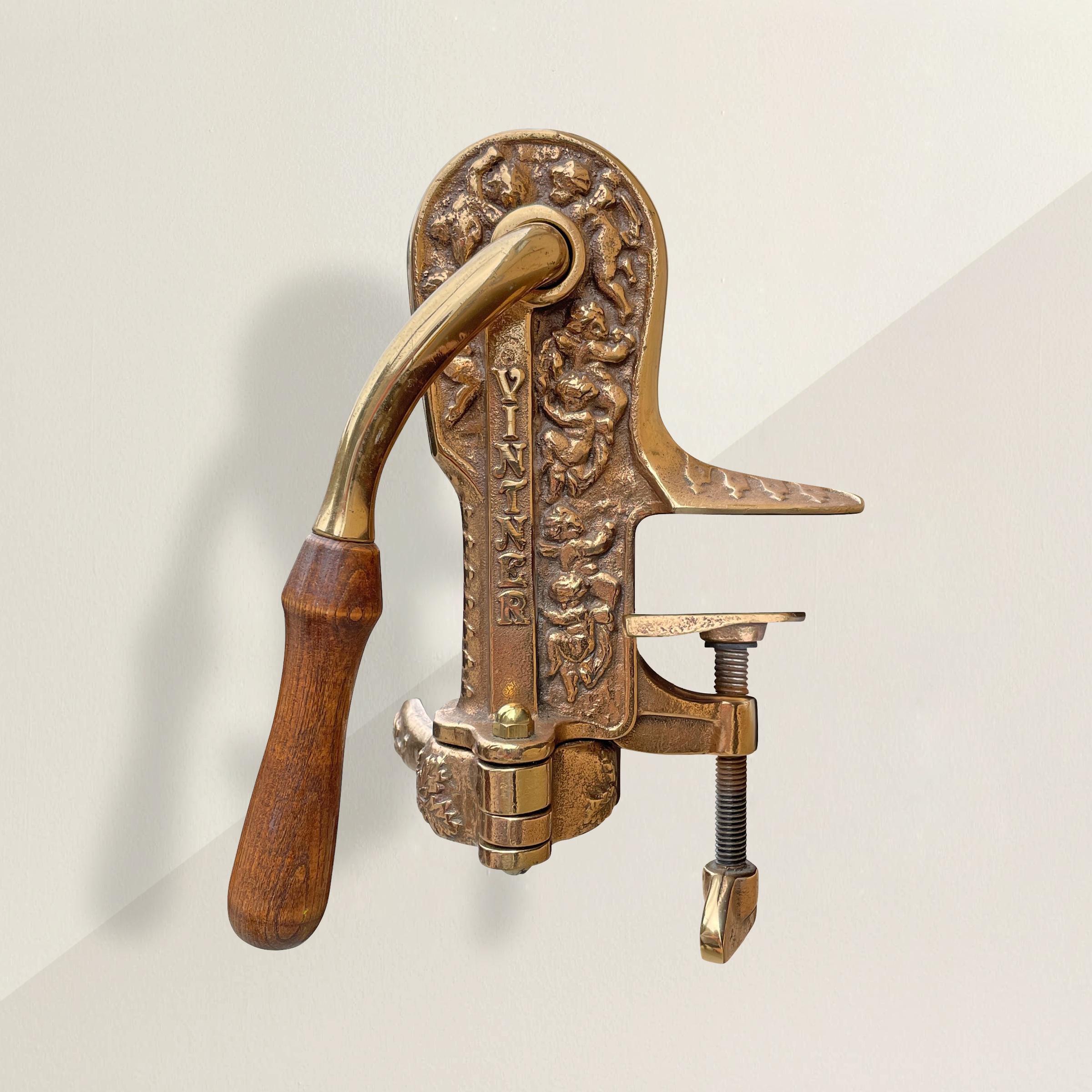 A wonderful 20th century American cast brass corkscrew that mounts to a table top, and features chubby cherubs and grape leaves. Top operate, one places the neck of the bottle in the clamp, pull the handle up to engage the corkscrew, and pull the