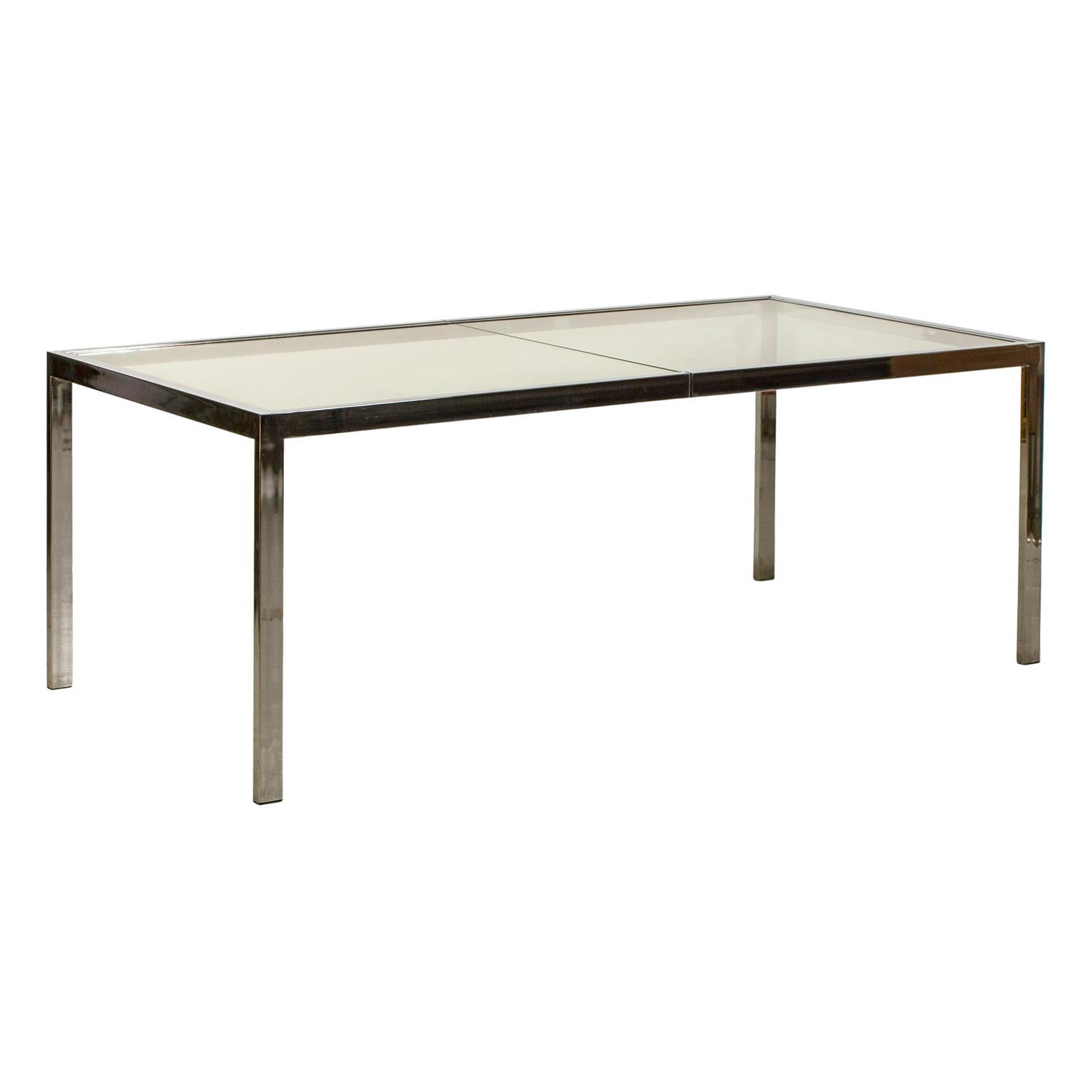 A large, vintage Mid-Century Modern American extendable dining table made of handcrafted chrome, designed by Milo Baughman in good condition. The table comes with two metal and glass plate extension; the glass top is supported by metal fittings.
