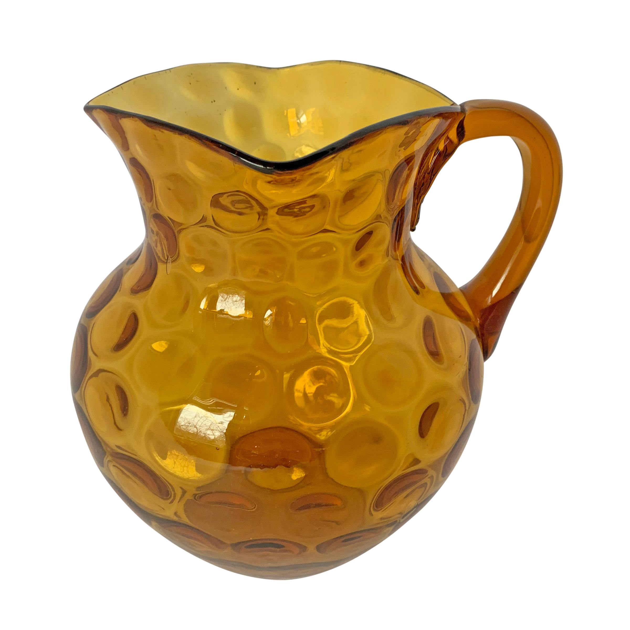 A fanciful early 20th century American amber glass pitcher covered polka dotted dimples with a pulled and applied handle. This pitcher also makes a beautiful flower vase.