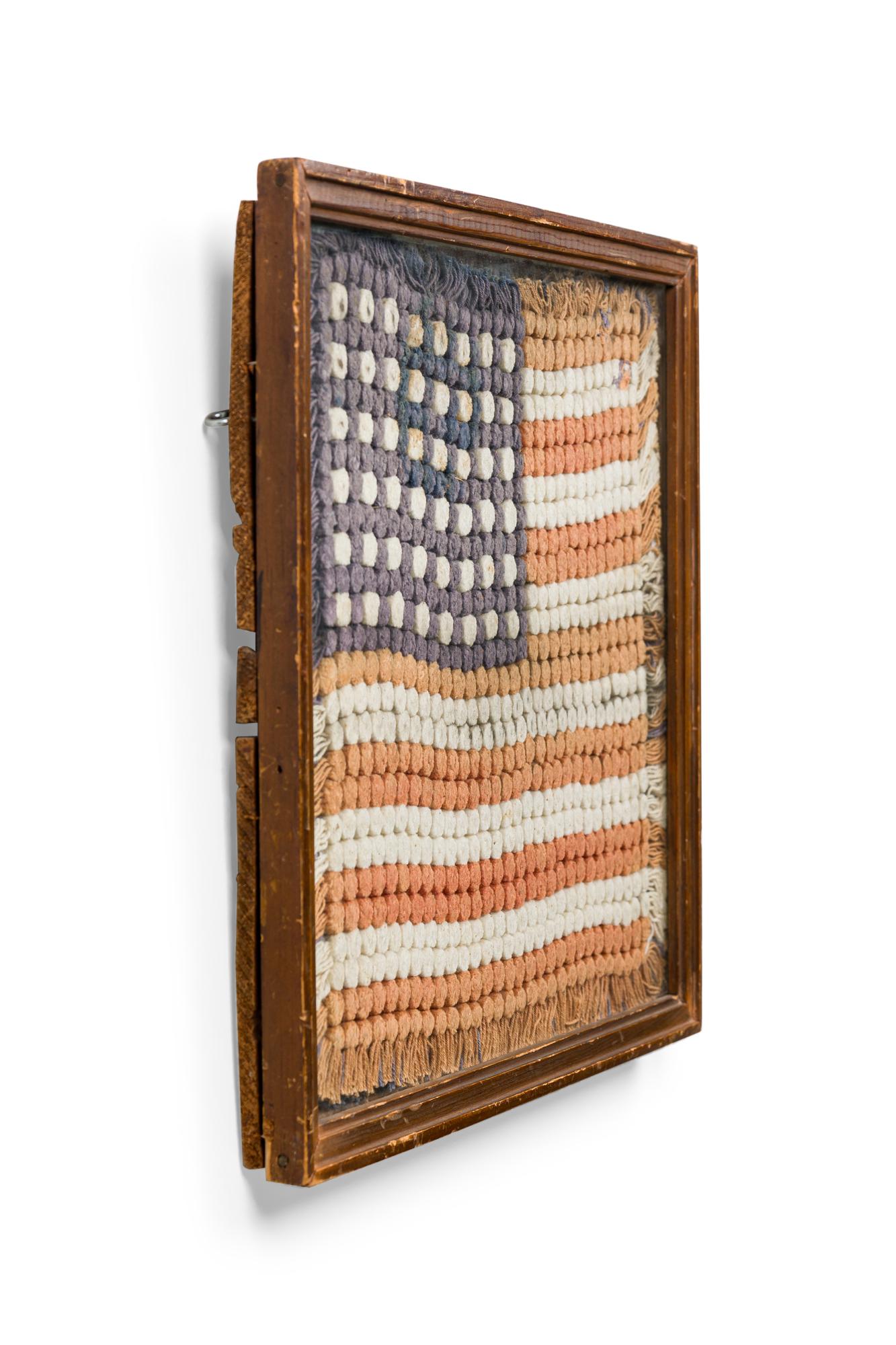 American Country (early 20th Century) folk art embroidery of a US flag portrayed with small pompoms in a wood frame behind glass.