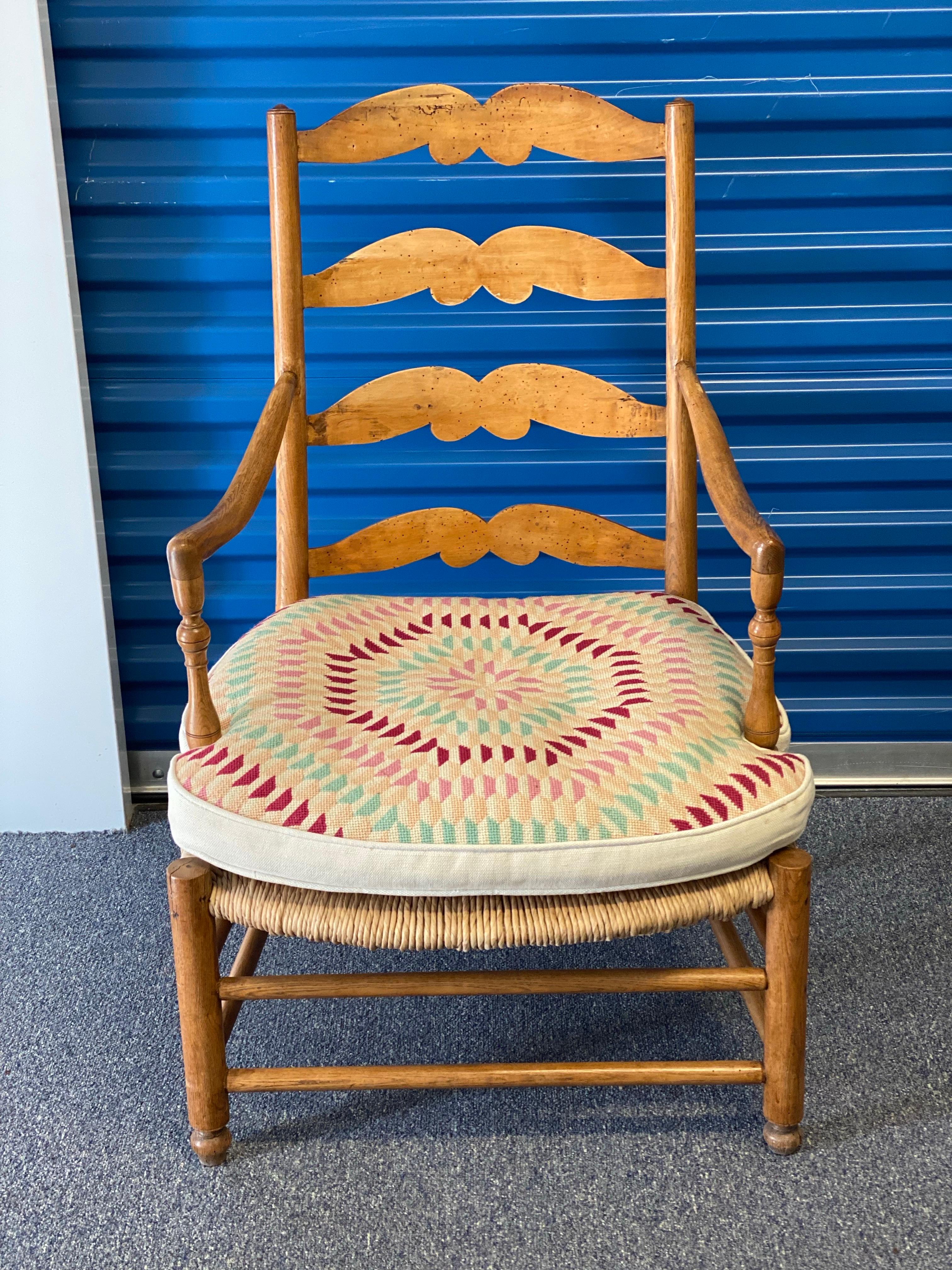 20th Century American Ladder Back Armchair with Rush Seat and Needlepoint Cushion.
This American ladder-back armchair is a quintessential example of early American craftsmanship.  The chair features a simple yet elegant design with turned spindles