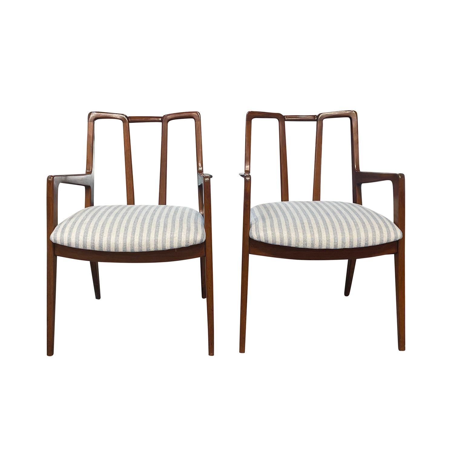 A vintage Mid-Century modern American pair of armchairs made of hand crafted polished Walnut, designed and produced by John Stuart in good condition. The detailed dining room chairs have an open, inclined sculptural backrest with arched arms,
