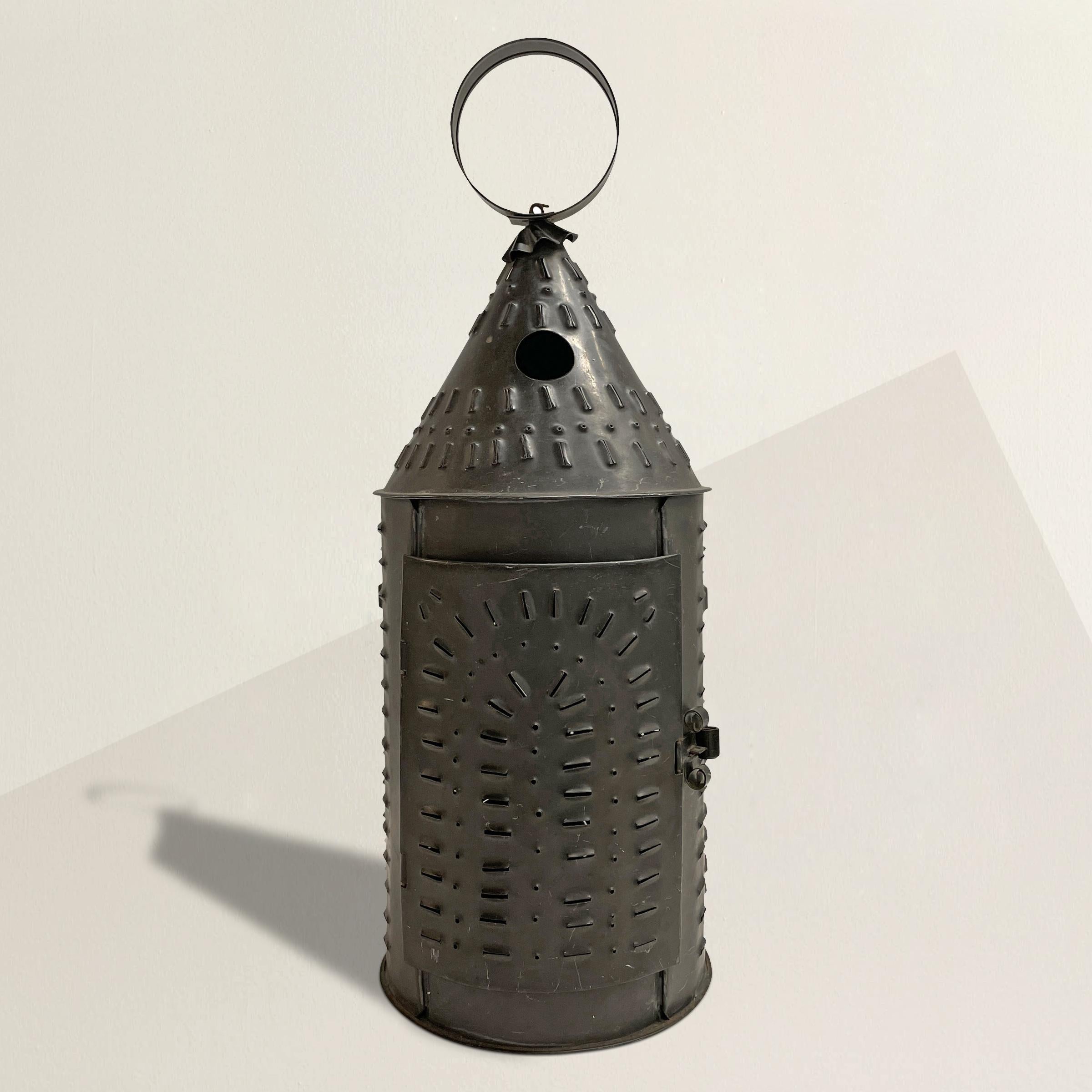 A charming 20th century American punched tin candle lantern with simple geometric pattern, a ring for hanging, and a door for accessing the candle. The lantern is currently used with a candle, but it would be fairly simple to have it wired.