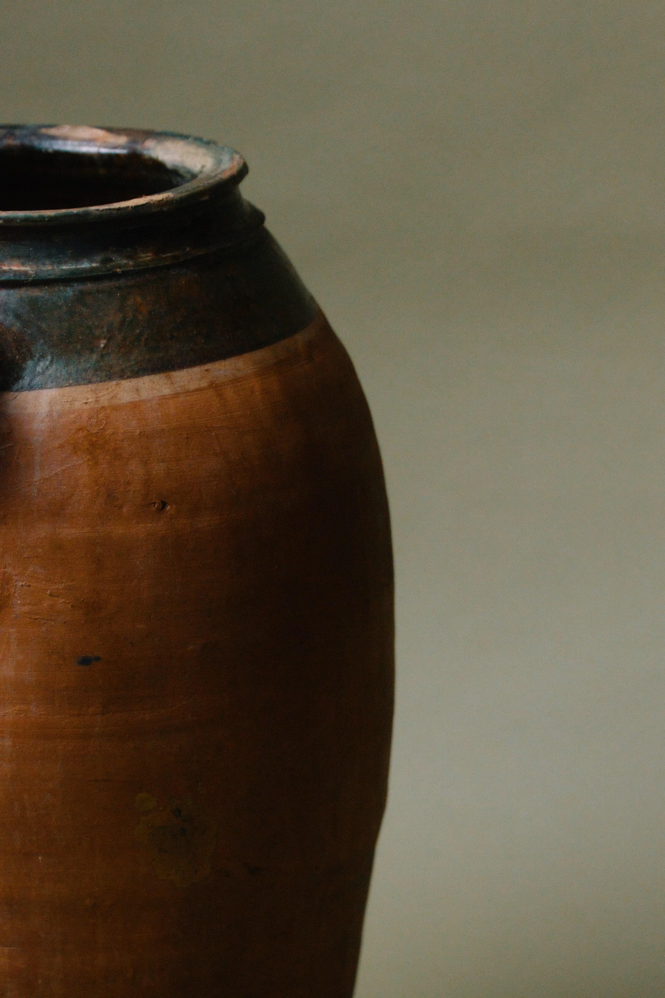 Questo vaso in terracotta anatolica del XX secolo si distingue per l'elegante bordo smaltato di verde, un dettaglio vibrante che completa la base in terracotta rustica. Realizzato in Turchia, questo vaso un tempo serviva come recipiente funzionale