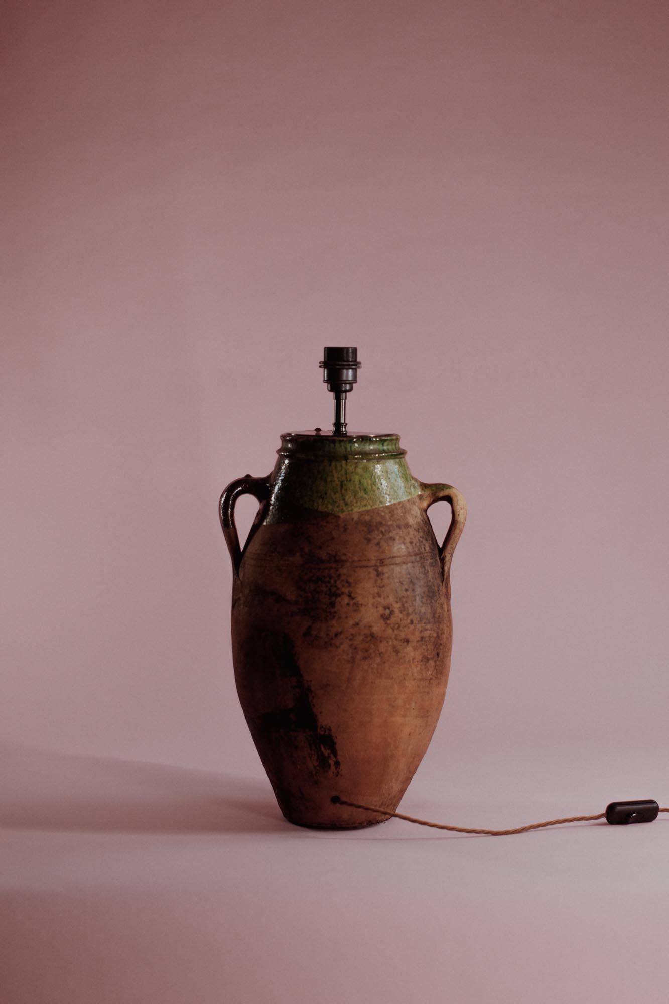 This 20th-century Anatolian terracotta pot embodies the essence of traditional craftsmanship with its twin-handled design and distinctive green-glazed rim. Once a functional vessel for storing liquids, it now serves as an elegant decor piece that