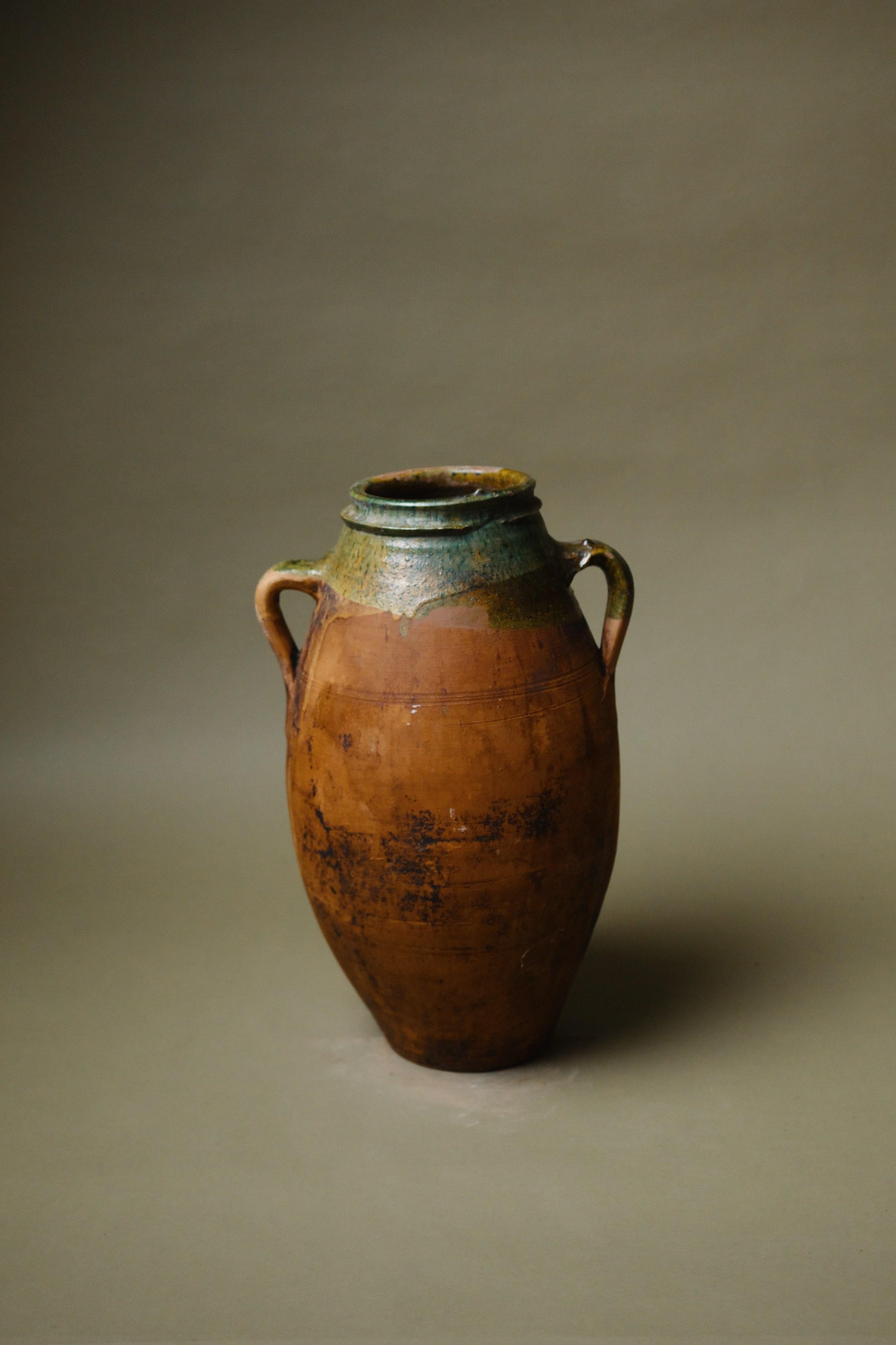 Ce vase en terre cuite d'Anatolie du XXe siècle incarne l'essence de l'artisanat traditionnel avec son anse double et son bord distinctif à glaçure verte. Autrefois récipient fonctionnel pour stocker des liquides, il sert aujourd'hui de pièce de