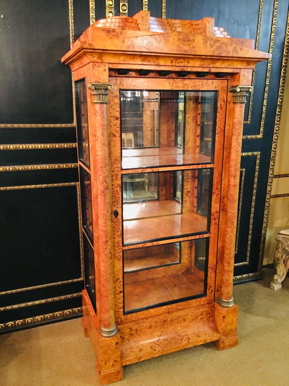 Bird’s-eye maple root veneer on solid pinewood, one-drawered curving border-case on plinth-feet. Architecturally bowed front flanked with full columns from solid beech. Carved and hand painted capitals and bases. On three sides.