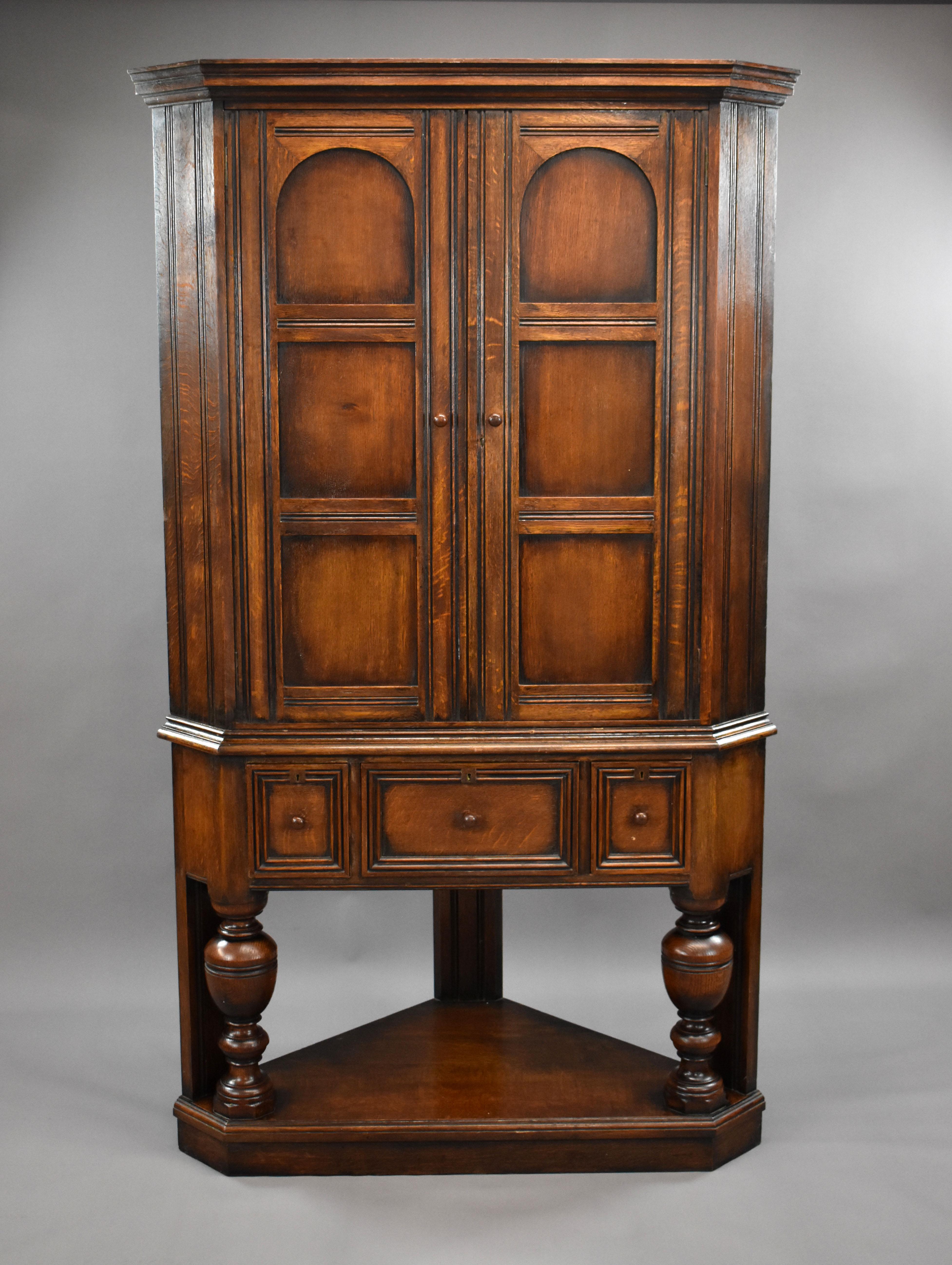 For sale is a good quality solid oak corner cupboard by Liberty & Co, London. Having two paneled doors, opening to reveal two shelves, the cupboard sits above three oak lined and hand dovetailed drawers. The cupboard stands on three legs, the front