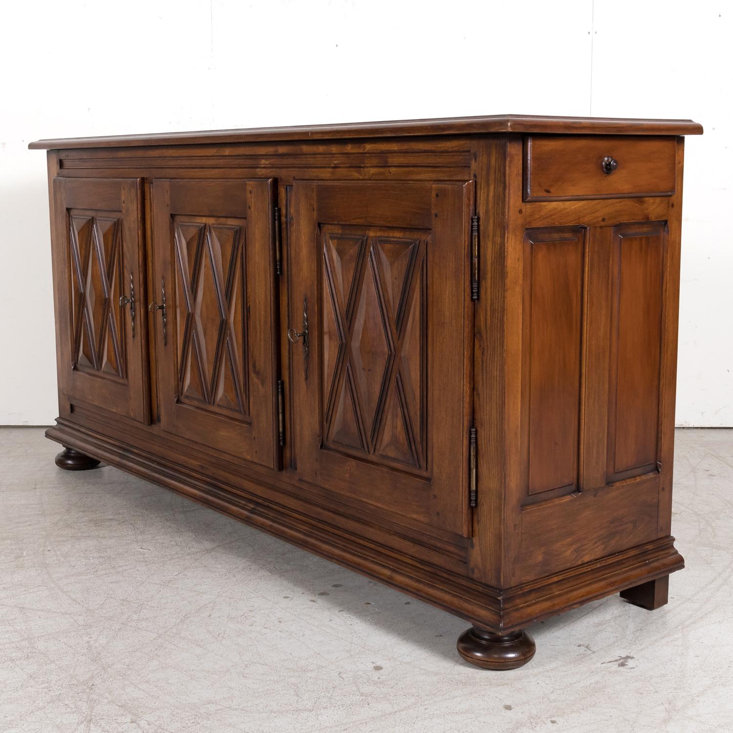 An antique French Country Louis XIII style carved enfilade buffet handcrafted of solid chestnut in Normandy, circa 1920s, having an inset rectangular plank top over three doors with raised diamante point decoration that open to reveal a single