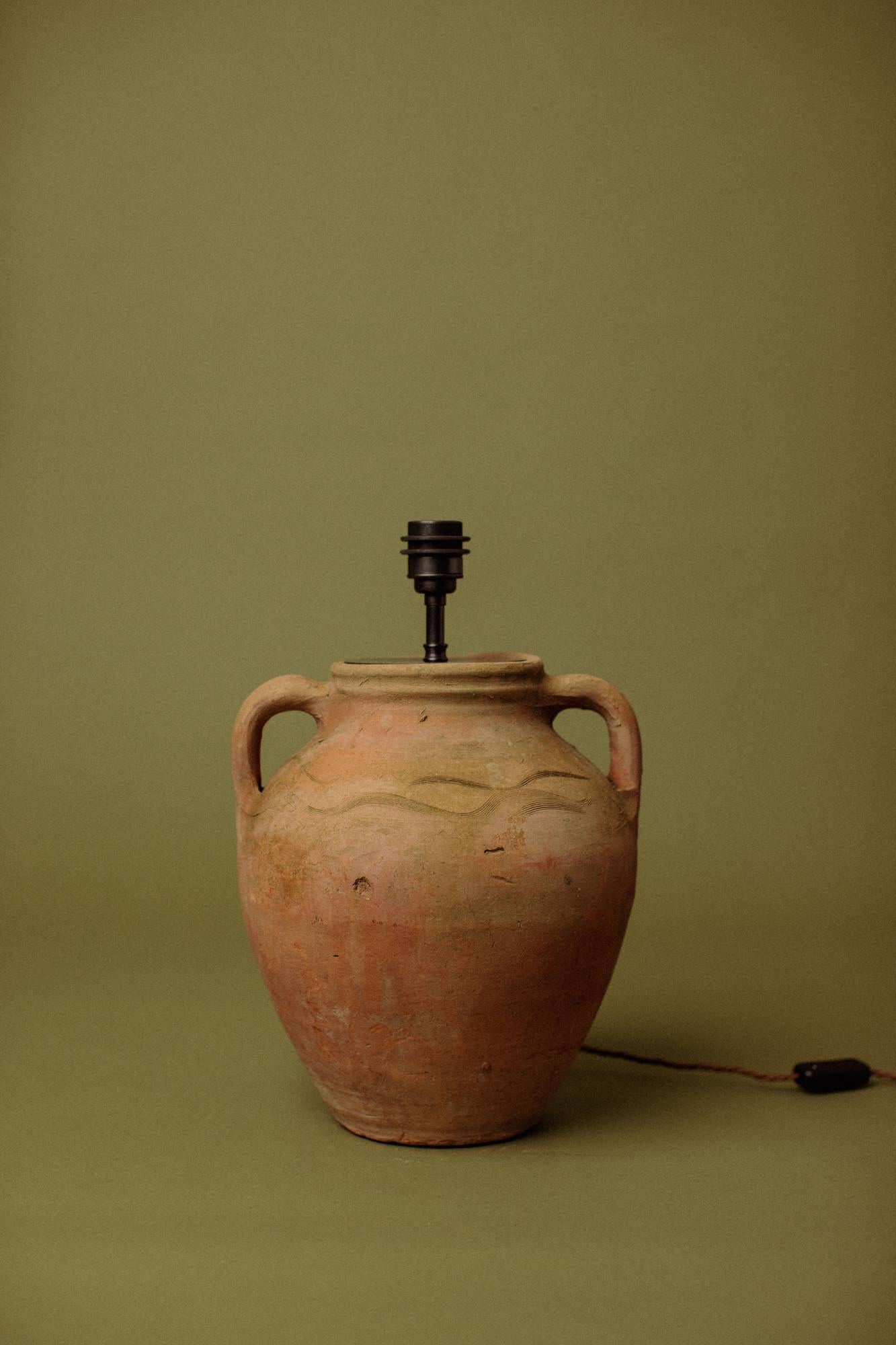 Cette lampe de table en terre cuite façonnée à la main au XXe siècle transforme une jarre utilitaire de stockage d'huile d'olive du sud de l'Anatolie en un éclairage raffiné. Moulé dans l'argile rouge grossière des contreforts de la région, le