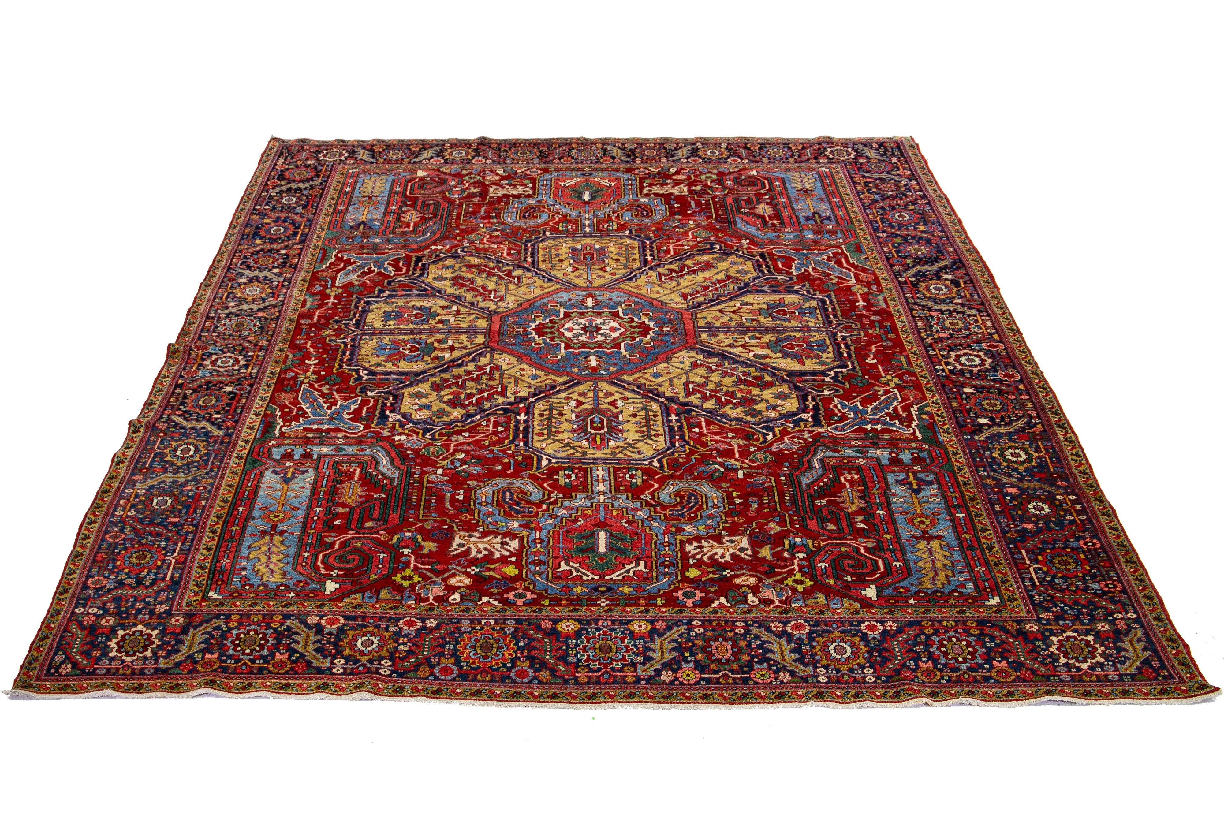 This is a beautiful antique Heriz hand-knotted wool rug featuring a red field. The Persian rug showcases a dark goldenrod center medallion motif and a multicolor allover design.

This rug measures 11' 1