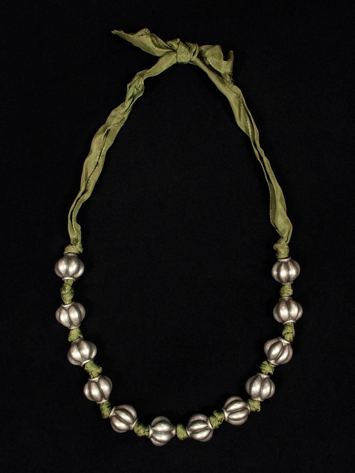 20th Century antique silver melon bead and green ribbon necklace

A handsome necklace of old Asian silver melon beads strung on a length of green silk grosgrain ribbon. Simple, eye-catching and light weight; 31 inches (79 cm) interior