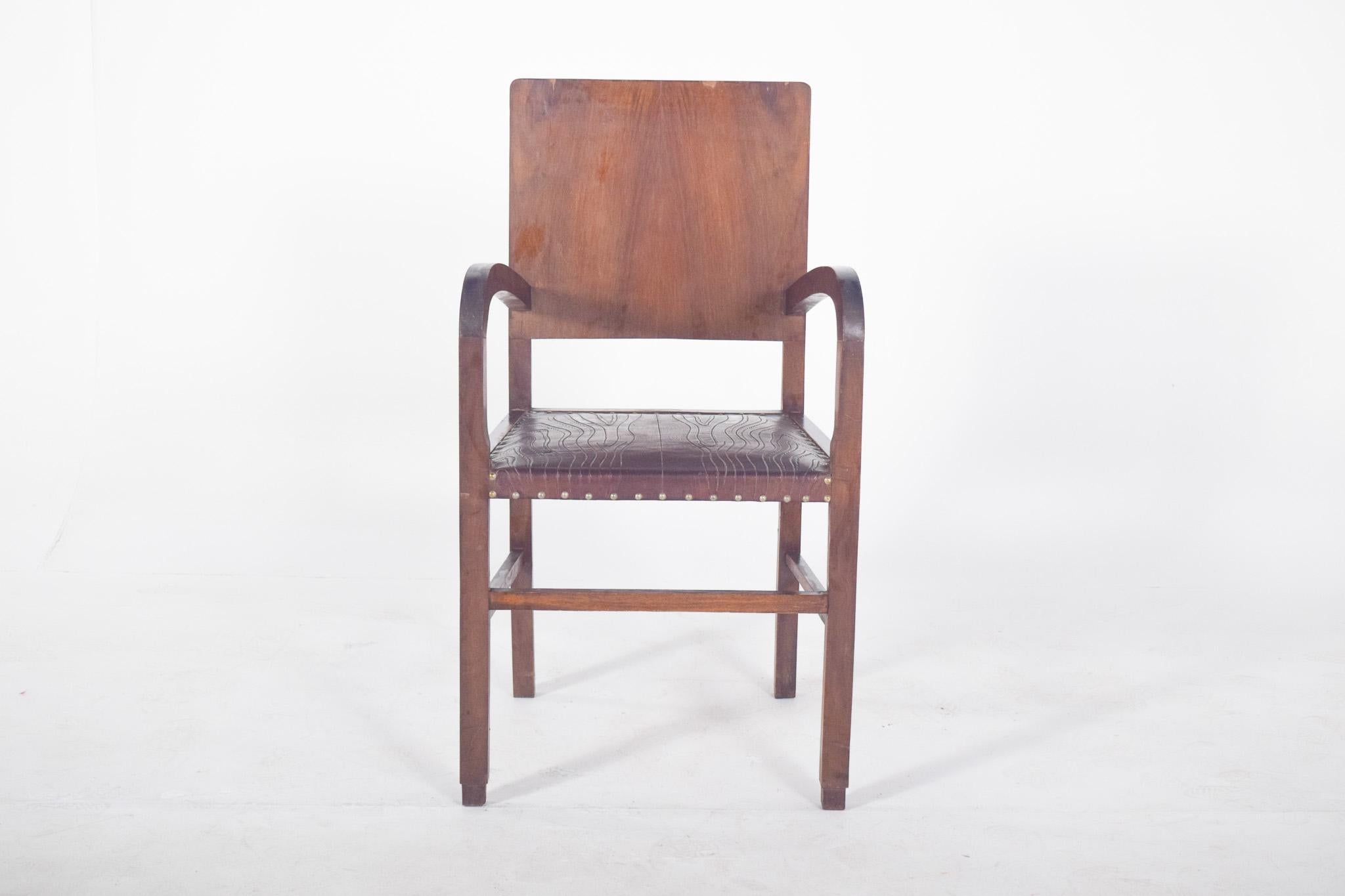 Fauteuil Art Déco. Avec ses accoudoirs incurvés et son dossier droit, il est représentatif du style Art déco, populaire entre les années 1920 et 1940. L'assise est recouverte de cuir brun foncé, avec des détails en bas-relief qui rappellent les