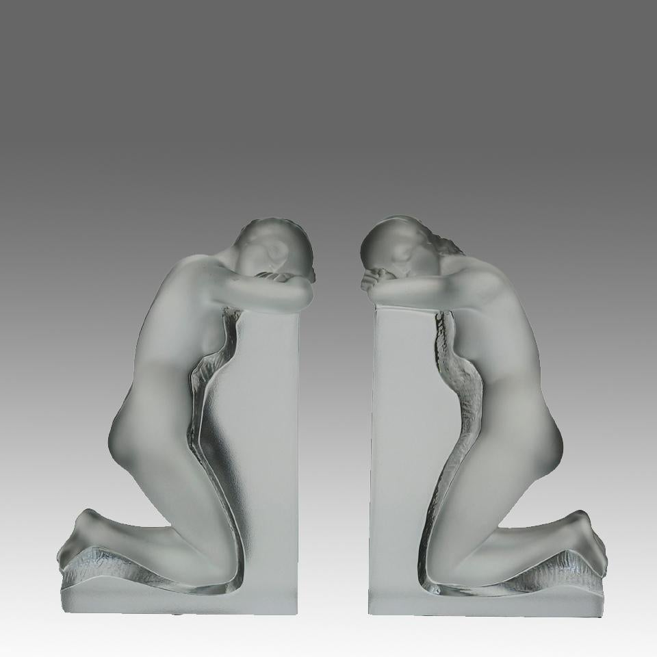 A very fine mid 20th Century frosted and polished glass pair of bookends modelle with figures of two naked beautys knelt down and resting against a wall with fine hand finished surface detail, both signed Lalique France

ADDITIONAL