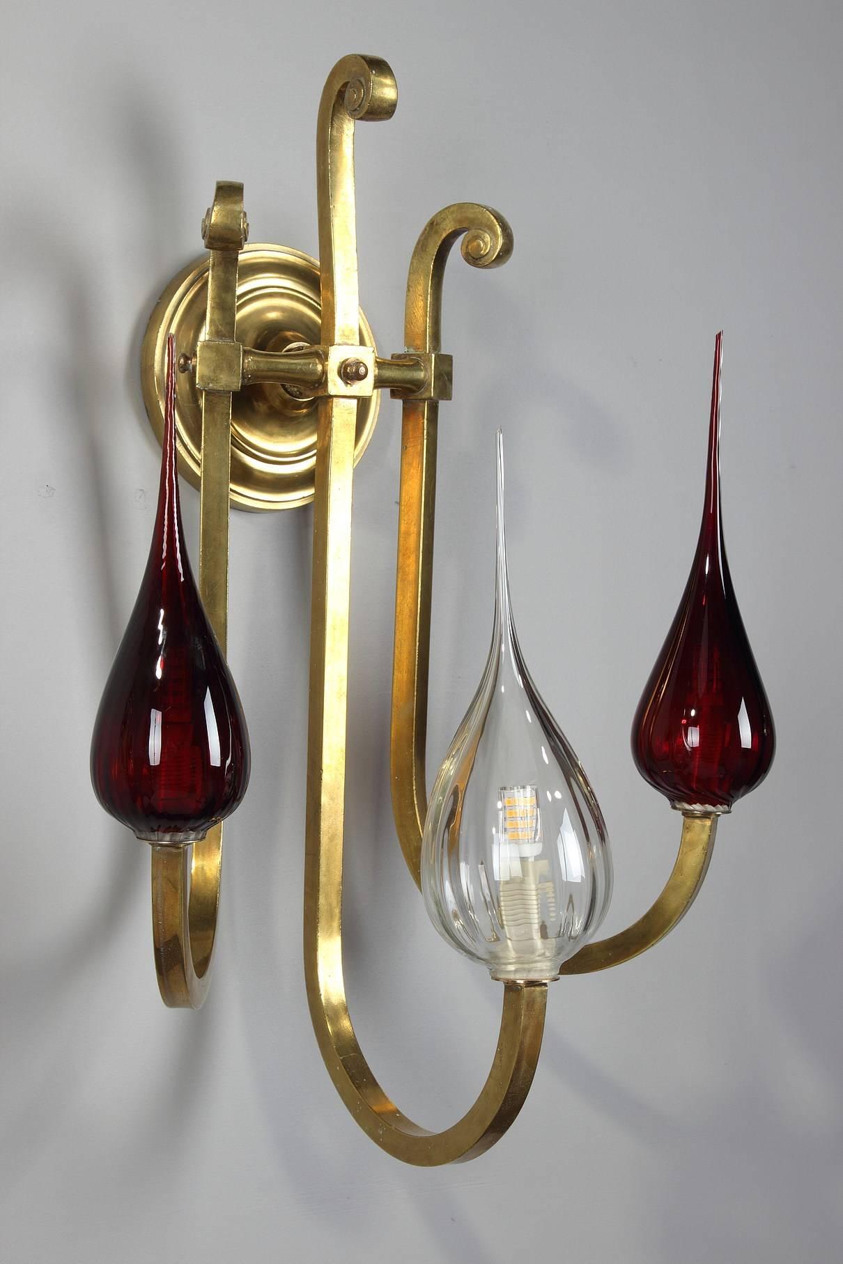 Gilded brass sconce with three scrolled arms of light fixed on the wall with a fluted rosette. Glass and red opaline drop-shaped globes. Art Deco mounts and contemporary glass globes,

circa 1940.
Dimensions: W 14.2 inches, D 9.4 inches, H 21.7