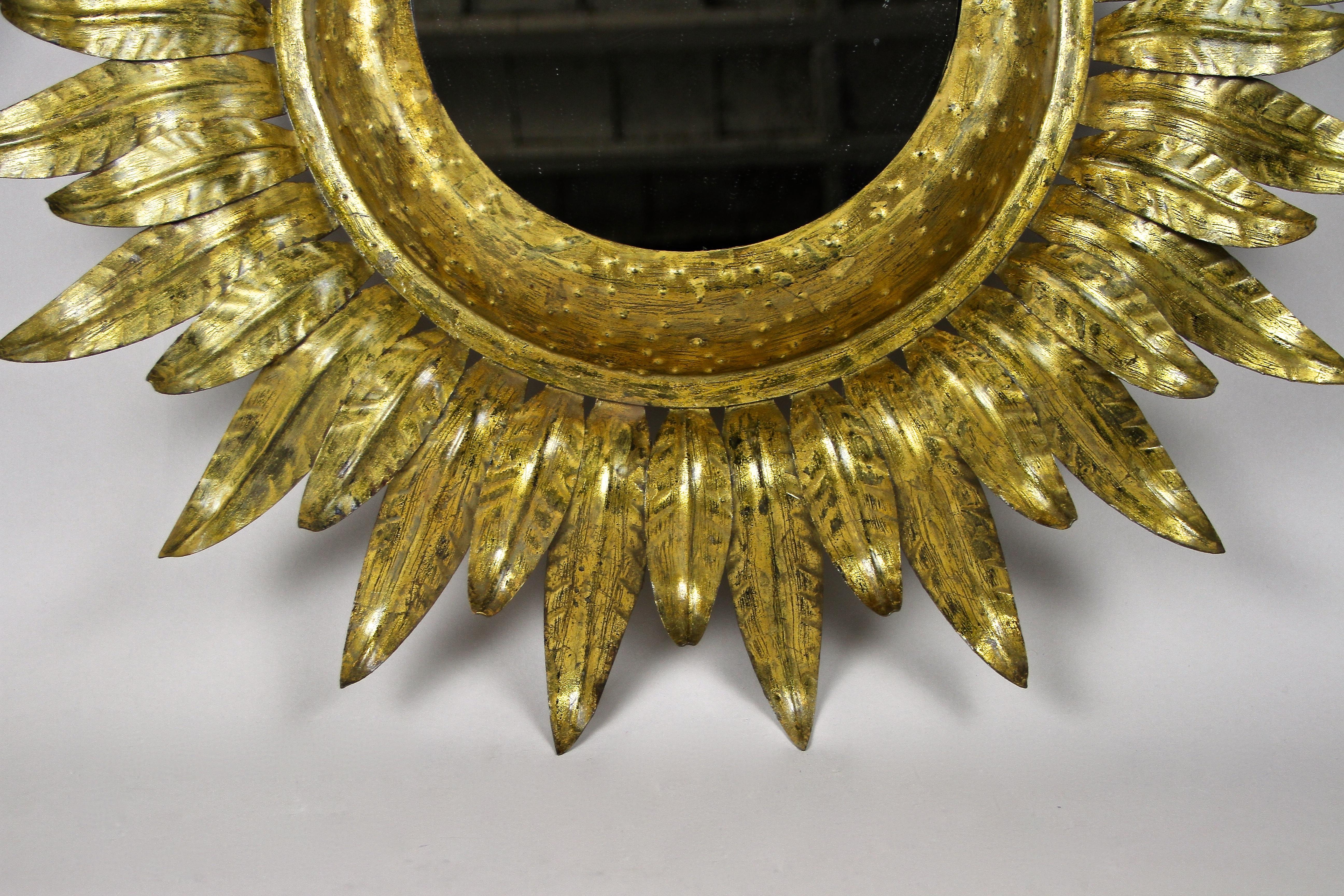 Sensational early 20th century sunburst wall mirror from the Art Deco period in France around 1920. This elaborately worked round mirror impresses with its artfully handcrafted foliage design made of composition gilt sheet metall. The gaps between