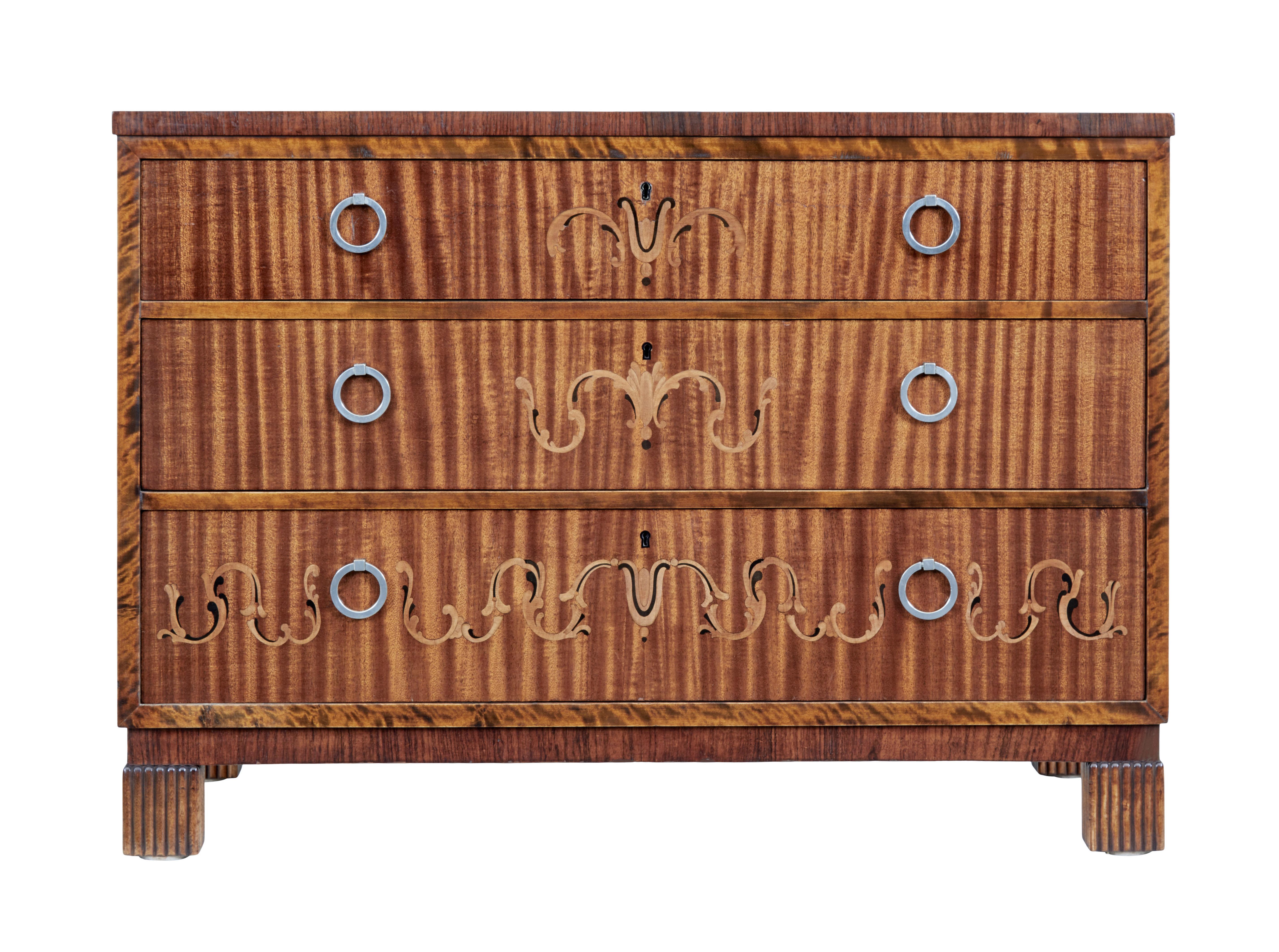 Swedish art deco chest of drawers, circa 1930.

Dark stained birch outer frame. 3 graduating mahogany drawer fronts inlaid with birch and ebonized swags, fitted with brush steel ring handles.

Standing on fluted block feet.

Minor surface