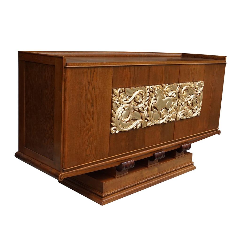 A vintage sideboard designed by Christian Krass. This cabinet is an Art Deco piece composed of solid oakwood. The front is divided into three panels with very detailed giltwood relief carvings, including vines, flowers, leaves, horses, and birds.