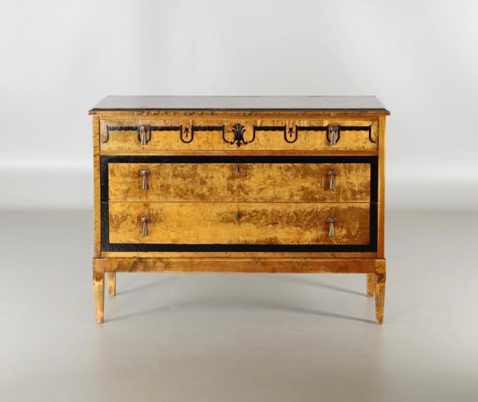 An Art Deco chest of drawers in birch wood, marquetry, with three drawers and handles in copper and brass, the birch wood has been painted with floral motifs and lacquered, the key is not available.,