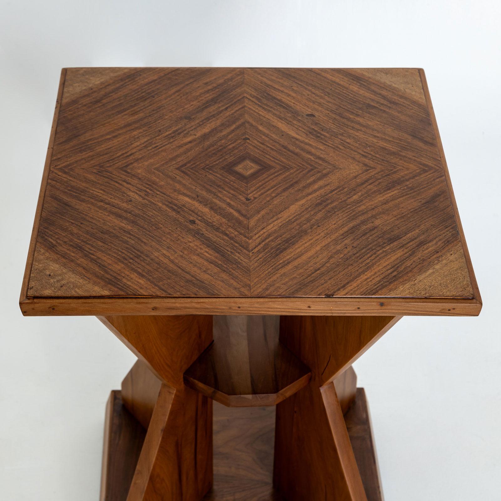 Elegant Art Deco side table in the characteristic hourglass shape with a square base and a retracted centre section. The table is made of walnut and has a charming, minimalist character.