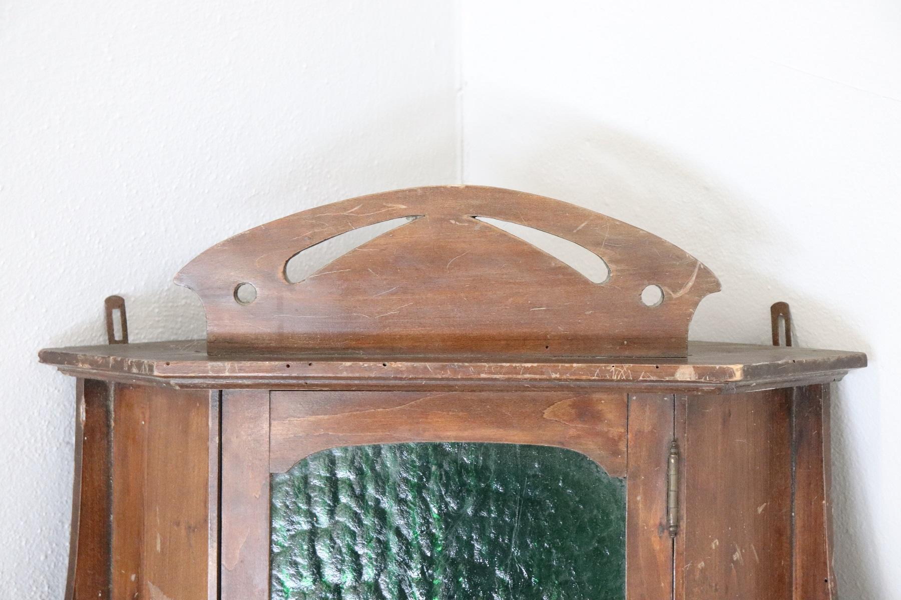 Italian small Art Nouveau corner cupboard about 1905. High quality furniture in solid Poplar. This corner unit needs to be fixed to the wall. Particular front door with antique green glass. On the sides, decoration with volutes of typical Art