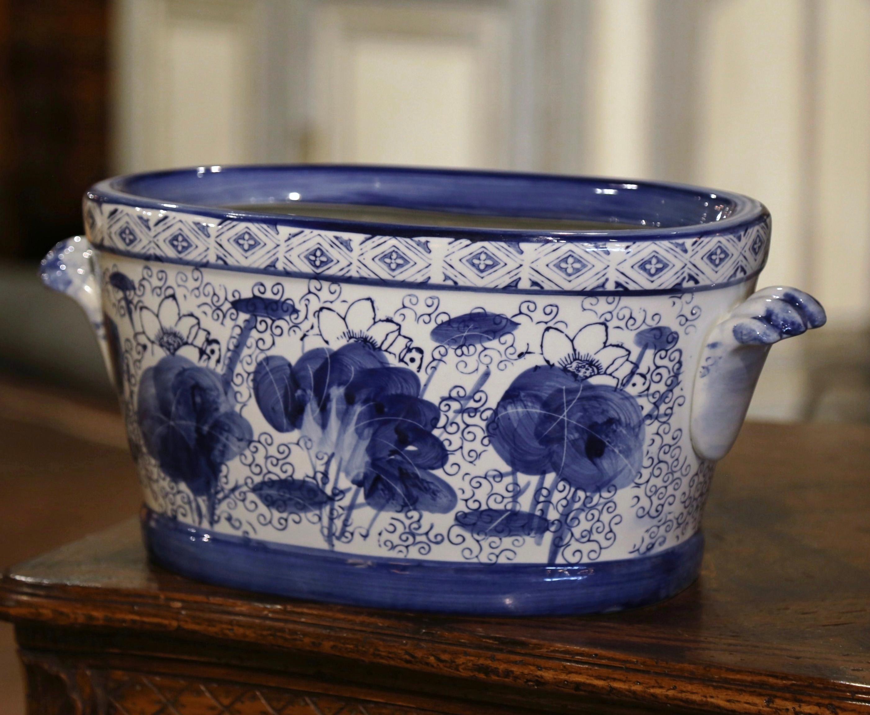 Crafted in Asian circa 1980 and oval in shape with bowed sides, the vintage porcelain basin is dressed with two shelf form side handles in high relief. The planter is decorated with hand painted floral and bird motifs around the perimeter of the pot