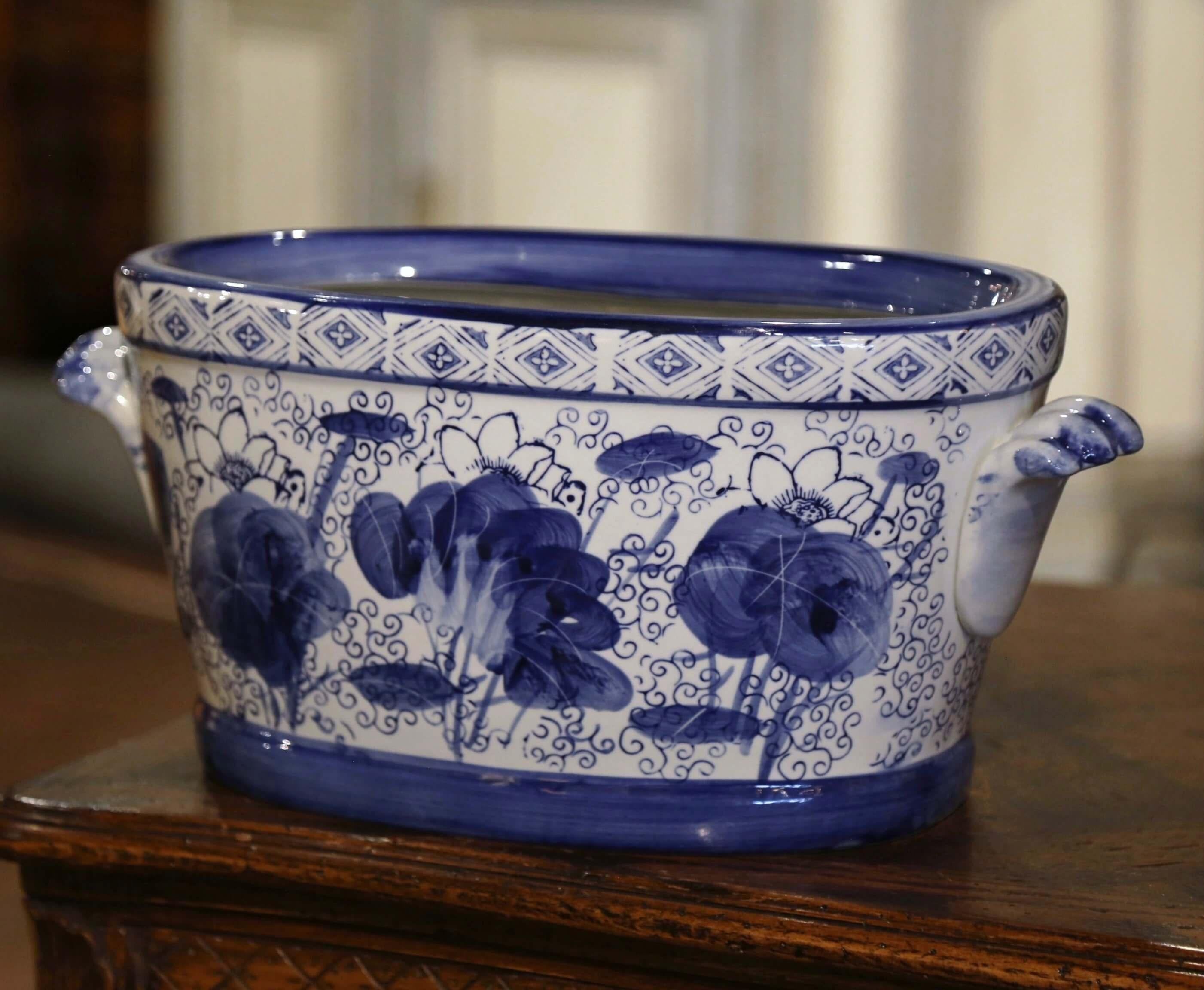 Crafted in Asian circa 1980 and oval in shape with bowed sides, the vintage porcelain basin is dressed with two shelf form side handles in high relief. The planter is decorated with hand painted floral and bird motifs around the perimeter of the pot