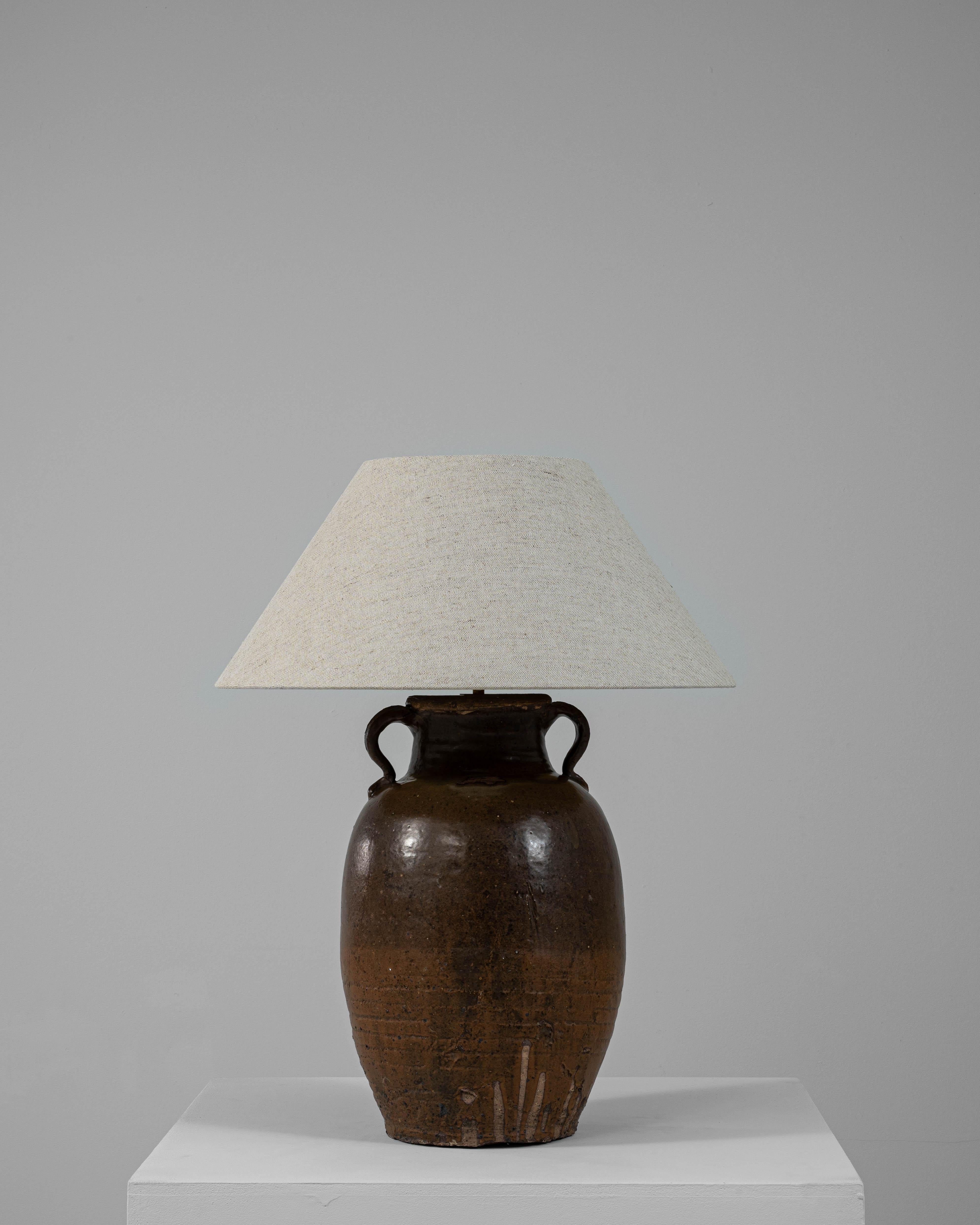 This 20th-century Asian ceramic table lamp features a traditional glazed jug base, distinguished by its rich brown tones and dual loop handles at the neck. The glaze reveals a subtle variation in texture and color, reflecting the artisanal