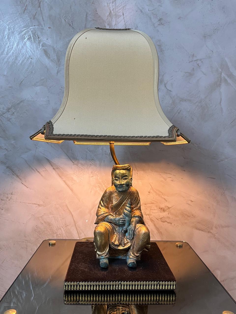 Elegant Asian-Style Brass Lamp with Fabric Shade

Add a touch of vintage charm to your interior with this unique Asian-style lamp. The finely crafted base features a seated figure in solid brass with an aged patina, combining gold and green tones