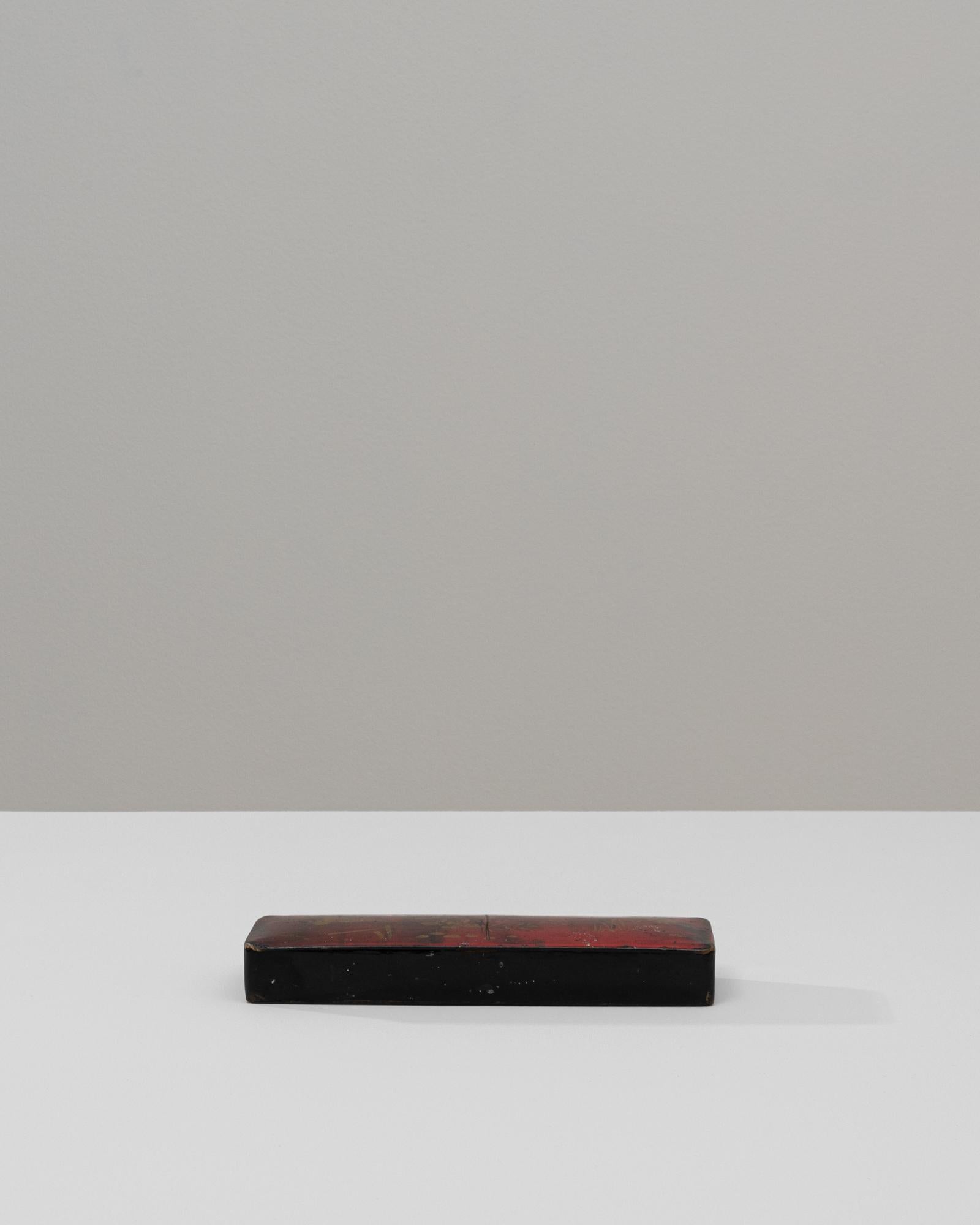 Cette boîte en bois asiatique du XXe siècle présente une forme rectangulaire raffinée, ornée de détails dorés réalisés à la main qui ressortent subtilement à travers sa laque usée par le temps. L'extérieur présente une riche finition rouge et noire,