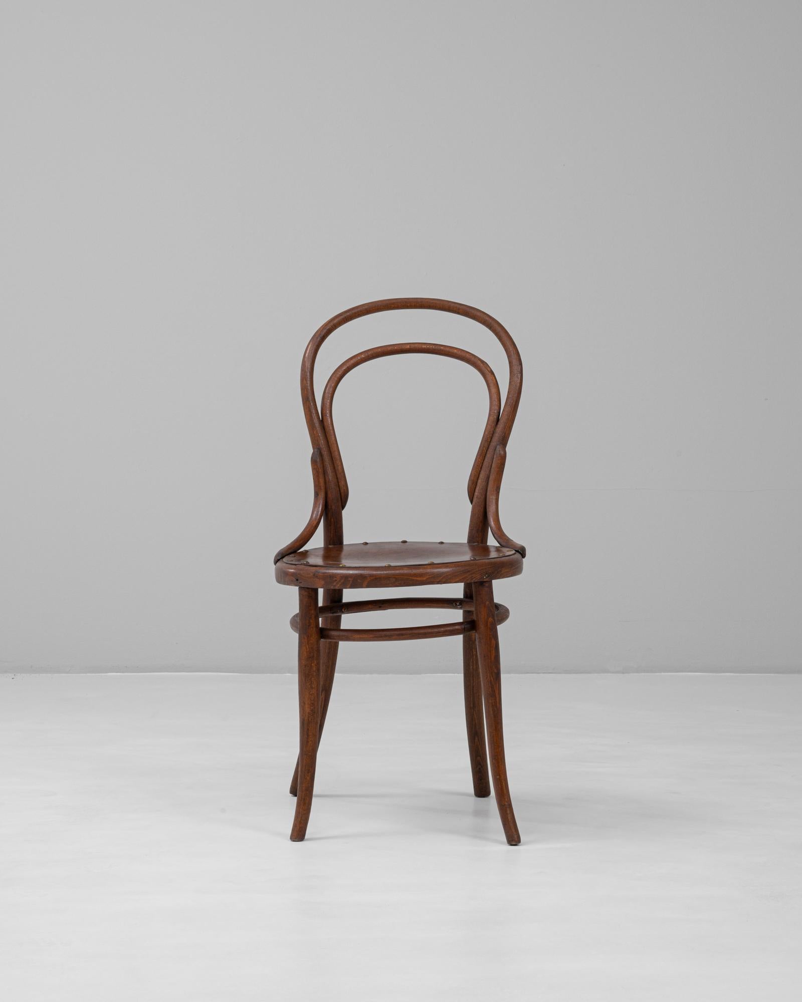 Esta silla de bistro de madera curvada austriaca del siglo XX encarna la perdurable elegancia y funcionalidad de los asientos clásicos de los cafés europeos. Fabricada en madera patinada, la silla tiene un asiento redondo sujeto con remaches de