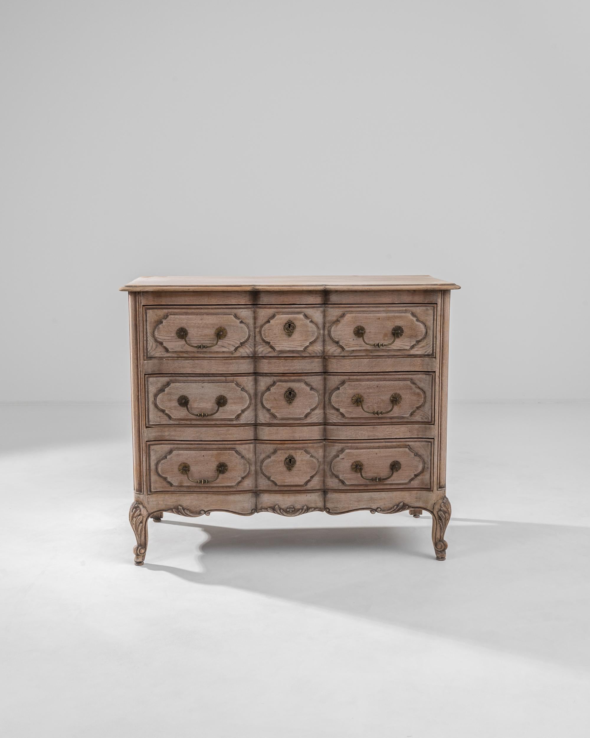Embark on a journey of timeless elegance with this 20th Century Belgian Bleached Oak Chest of Drawers. Standing gracefully on cabriole legs, this chest is a testament to exquisite craftsmanship and ornate detailing. The bleached oak finish lends it