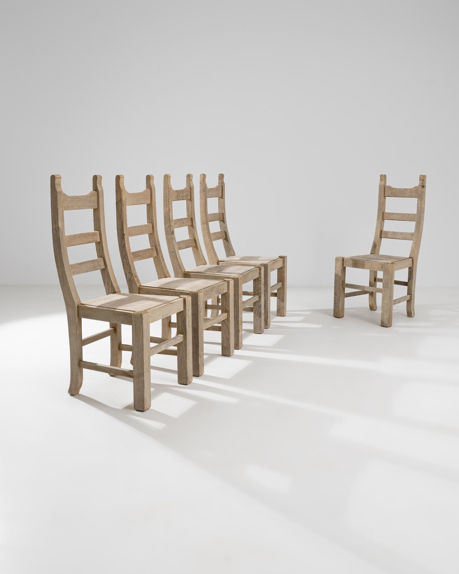 A set of wooden dining chairs from Belgium, circa 1960. Gently rounded chair seats, offset mortise and tenon spindles, and gracefully arched backs craft a set of chairs that are easy on the eyes. A careful refinishing process has enlivened the warm