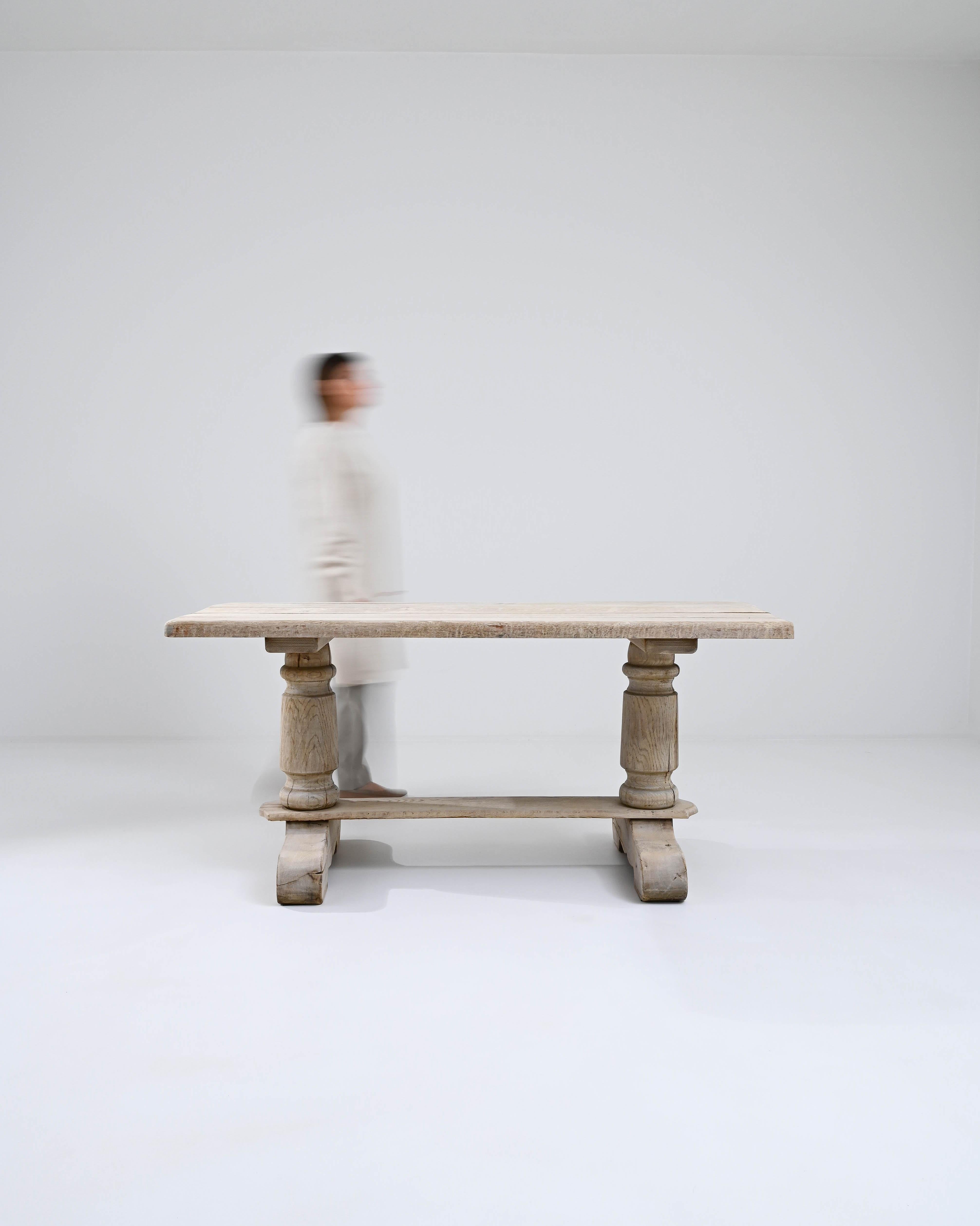 This 20th Century Belgian dining table is a testament to timeless craftsmanship and minimalist style. Crafted from bleached oak, its natural grain and soft, muted tones offer a serene dining experience. The table stands on robust, elegantly turned
