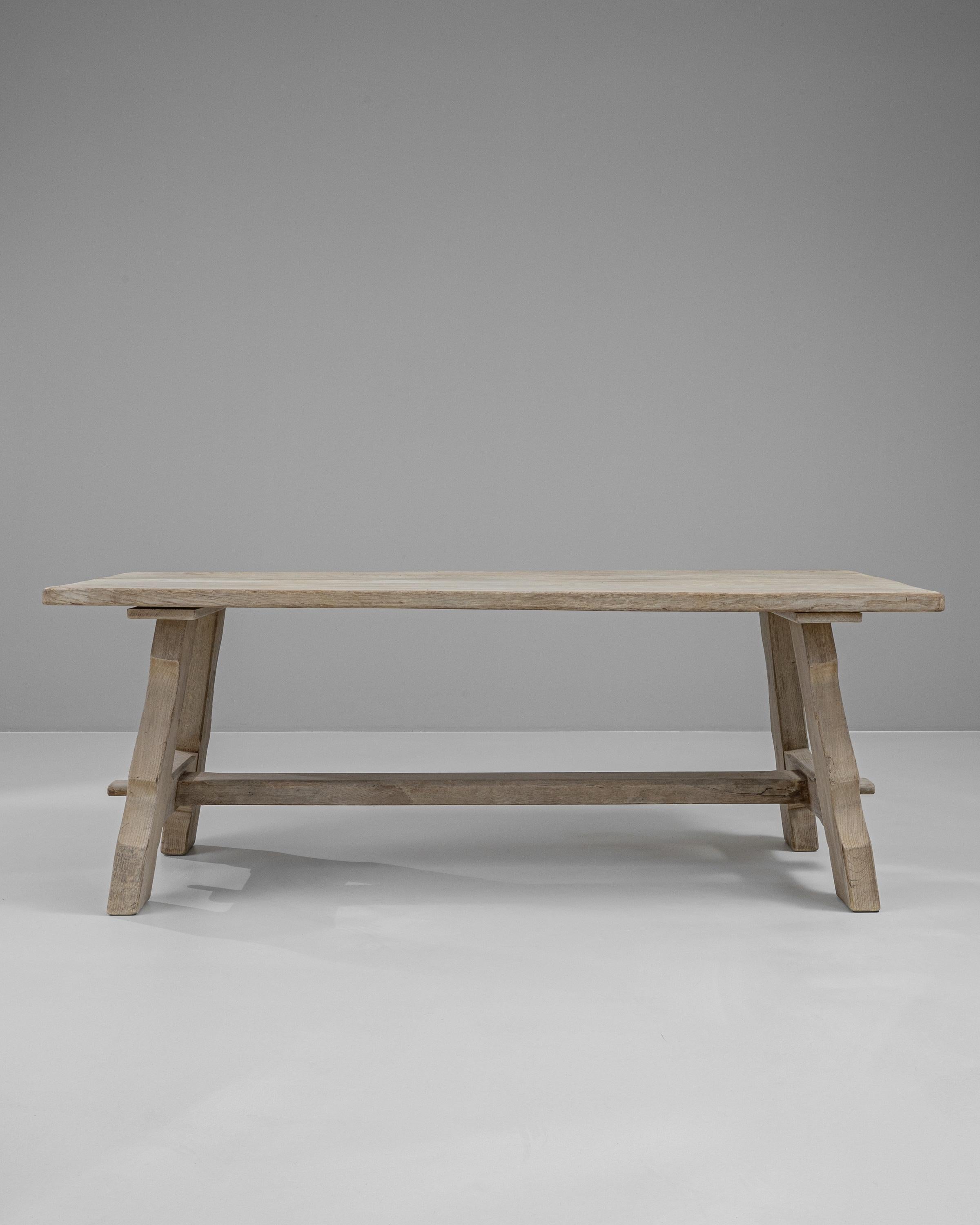 Bring rustic charm and robust craftsmanship into your dining room with this exquisite 20th-century Belgian dining table, expertly crafted from bleached oak. The table's sturdy design is highlighted by its unique trestle base, which features