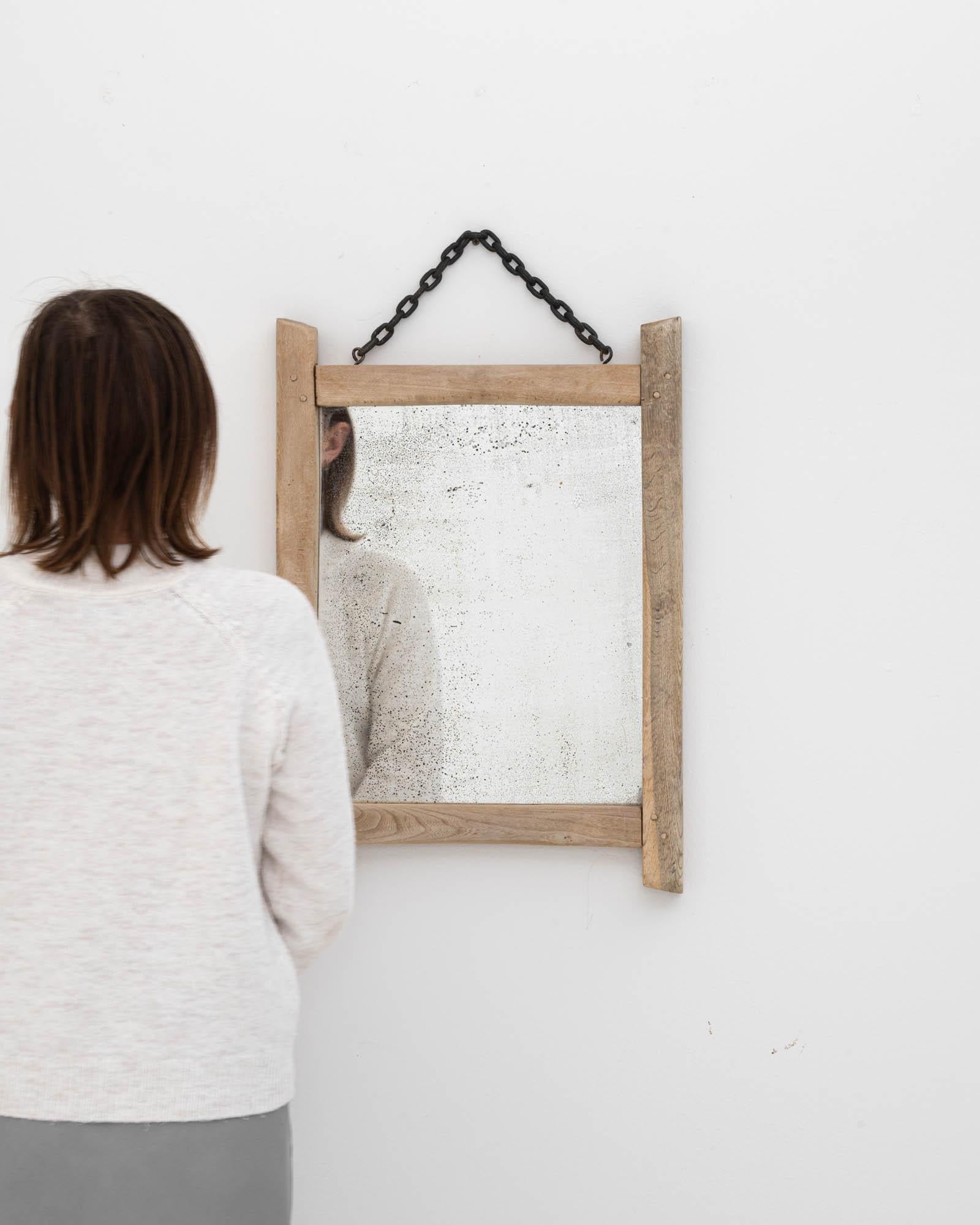 This 20th Century Belgian bleached oak mirror is a minimalistic and serene piece that captures the essence of rustic charm. The pale, washed-out wood frame, weathered by time, brings a light, airy feel to any space, while the simple black chain adds