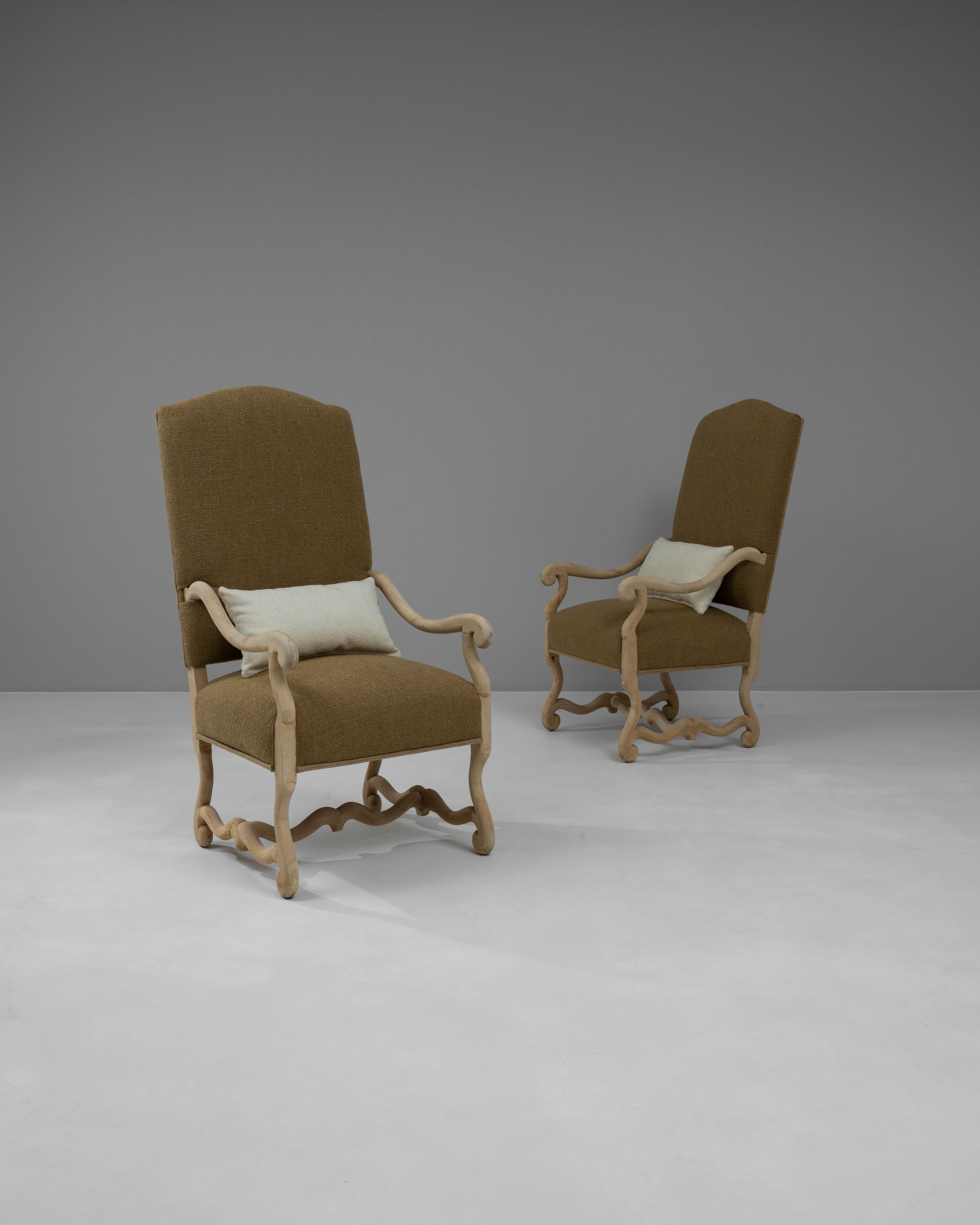 Elevate your living space with this exquisite pair of 20th Century Belgian armchairs, each crafted from bleached oak and meticulously upholstered in a rich, brown fabric. The chairs feature elegant, flowing lines and detailed carvings on the arms