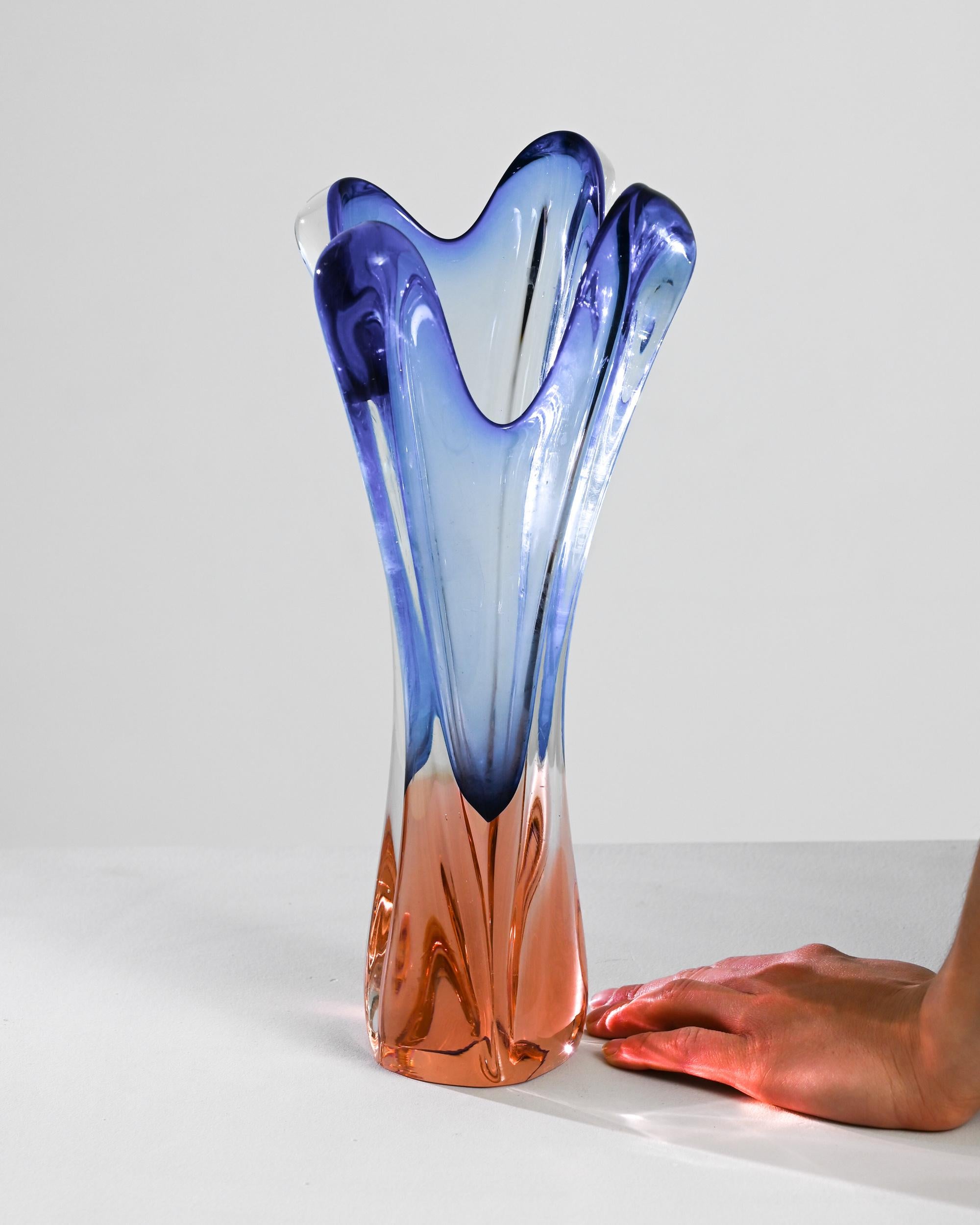 This 20th Century Belgian vase is an exquisite manifestation of glass artistry, showcasing a mesmerizing blend of blue and orange hues. Its unique form, reminiscent of a flame, rises with an elegant fluidity that is both dynamic and serene. The