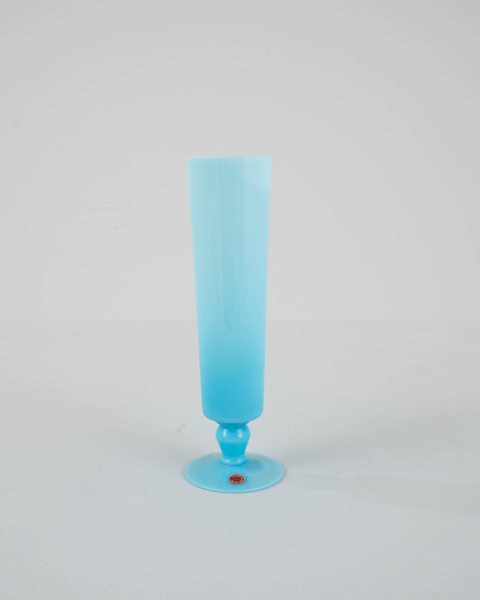 Indulge in the regal charm of this 20th Century Belgian Blue Glass Vase, a stunning embodiment of Belgian craftsmanship. Bathed in an enchanting ice blue hue, this vase captivates with its consistent and refined size. The regal base adds a touch of