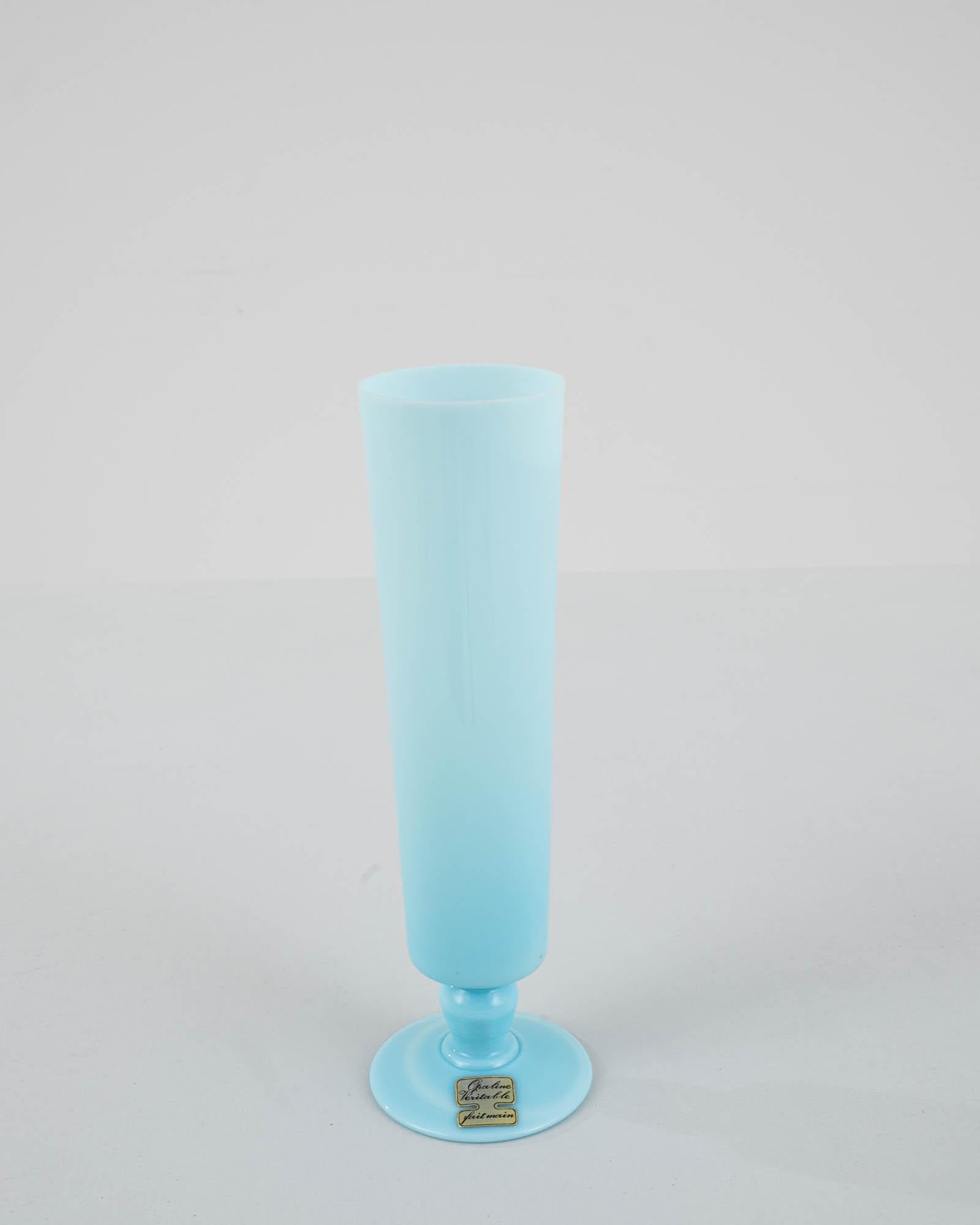 Indulge in the regal charm of this 20th Century Belgian Blue Glass Vase, a stunning embodiment of Belgian craftsmanship. Bathed in an enchanting ice blue hue, this vase captivates with its consistent and refined size. The regal base adds a touch of