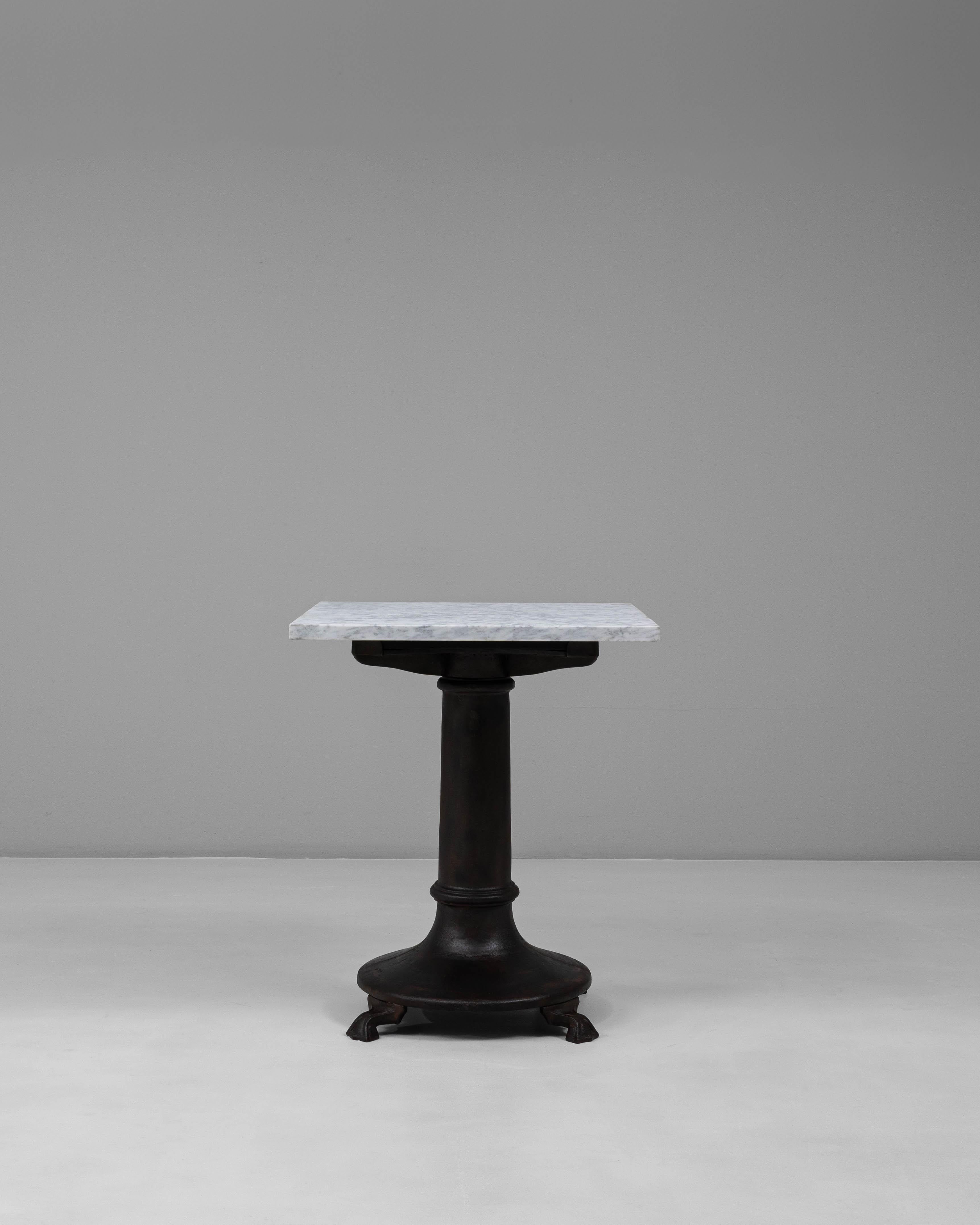 This 20th century Belgian bistro table combines durability with timeless charm, showcasing a cast iron pedestal base paired with a refined white marble top. The heavy cast iron base features a robust, flared column and claw-like feet, ensuring both