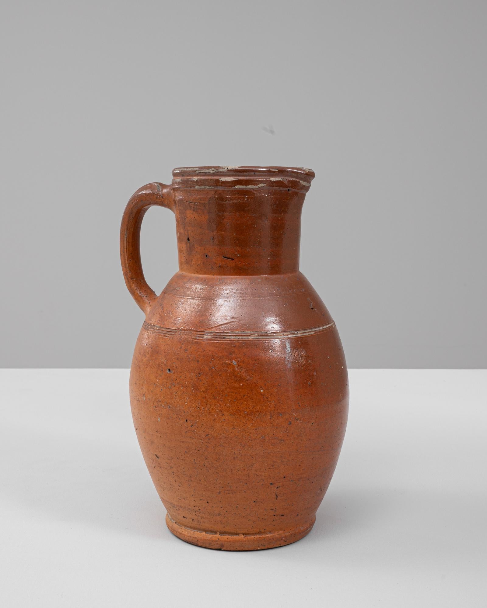 Questa brocca in ceramica belga del XX secolo cattura il calore e la funzionalità del tradizionale gres europeo. La sua silhouette classica - ampiamente arrotondata nel corpo e che si restringe in un collo alto e leggermente svasato - riflette una