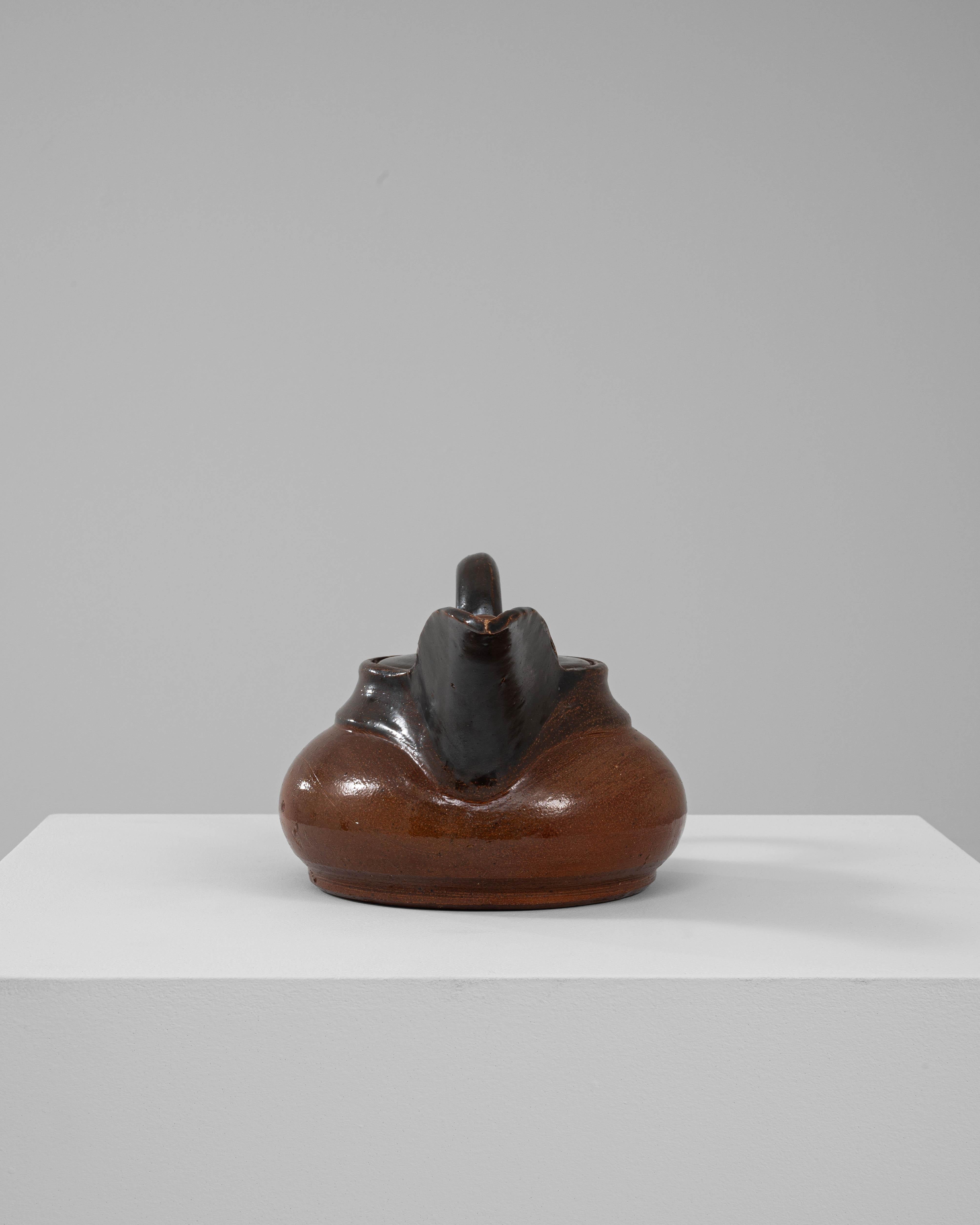 Cette charmante bouilloire belge en céramique du XXe siècle allie élégance rustique et design pratique. Dotée d'un corps lisse et arrondi dans un riche glaçage brun, la bouilloire est rehaussée d'un bec et d'une poignée d'un noir profond, créant