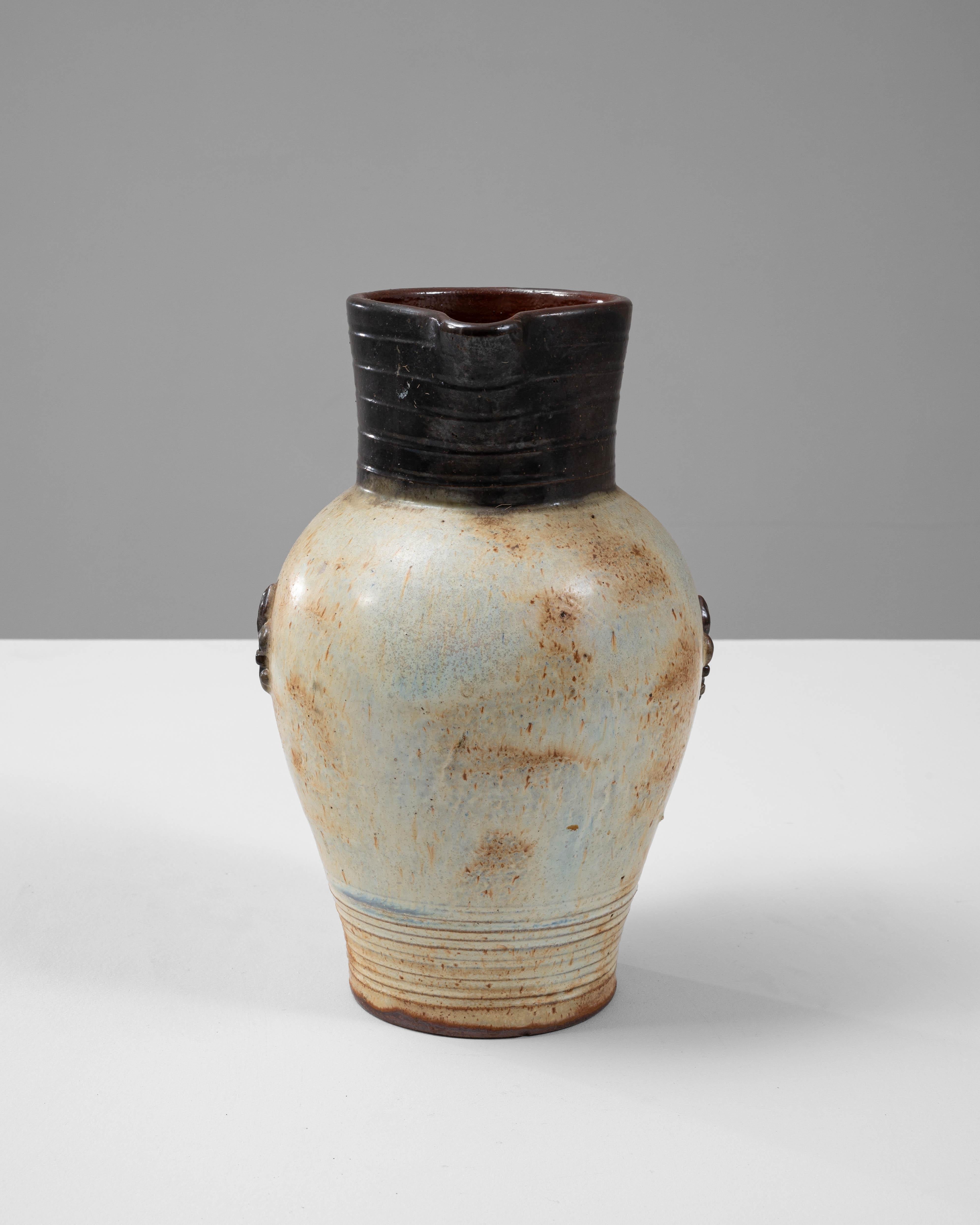 This elegant 20th-century Belgian ceramic pitcher by G. Losson beautifully combines artistry and functionality. The softly rounded body is adorned with a speckled cream glaze accented by warm, earthy tones, while the top and handle are finished in a