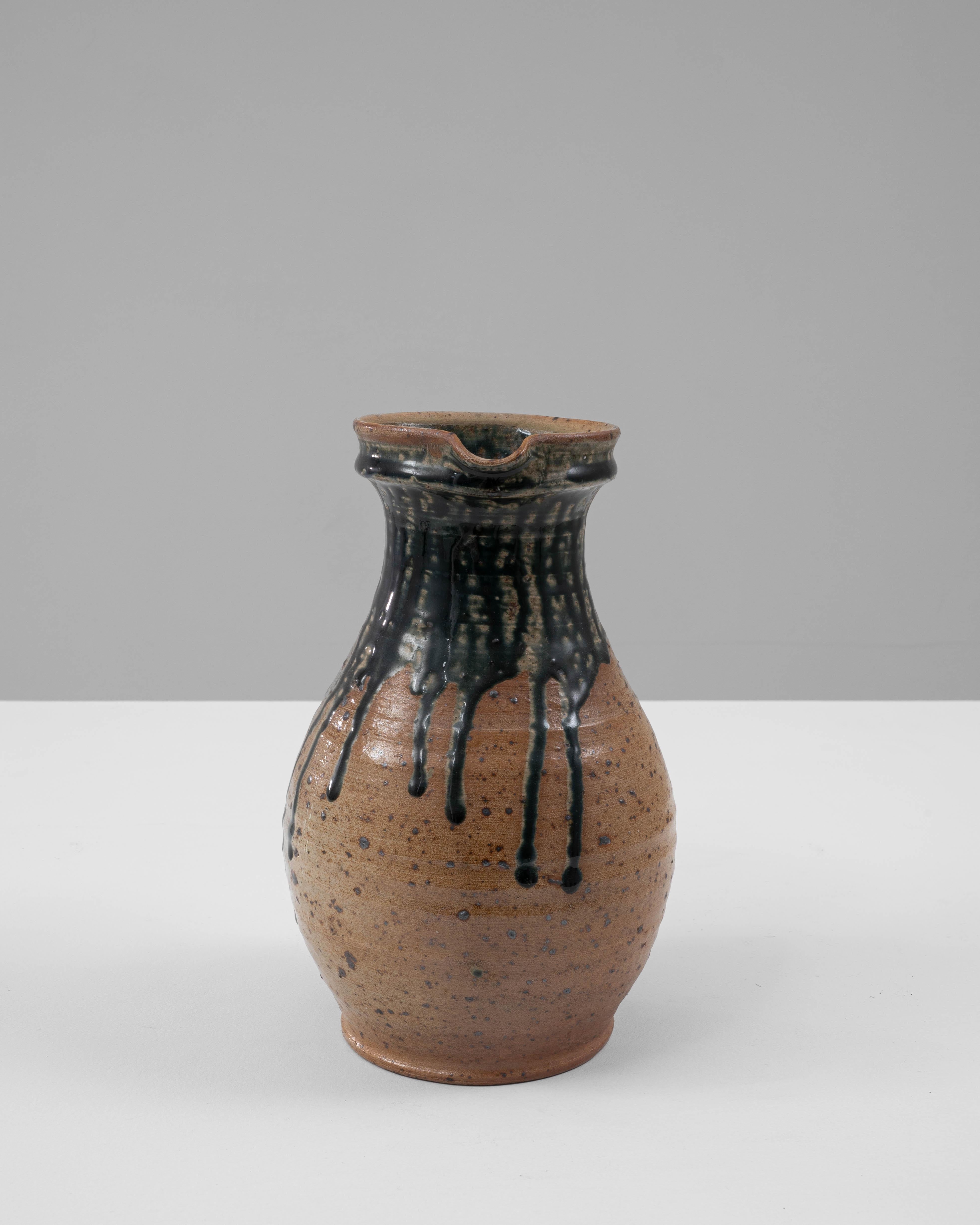 Questa brocca in ceramica belga del XX secolo, opera di G. Losson, è una miscela sorprendente di fascino rustico e dettagli artistici. La sua forma arrotondata è caratterizzata da uno smalto caldo e screziato nei toni della terra, accentuato da un