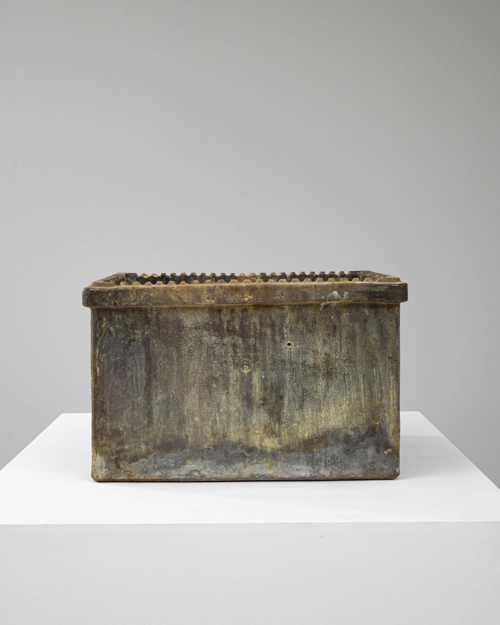 This 20th-century Belgian ceramic planter is a masterpiece of rustic charm and understated elegance. Rectangular in shape, it is adorned with a richly textured rim that offers a tactile contrast to its smoothly worn sides. The patina, a complex